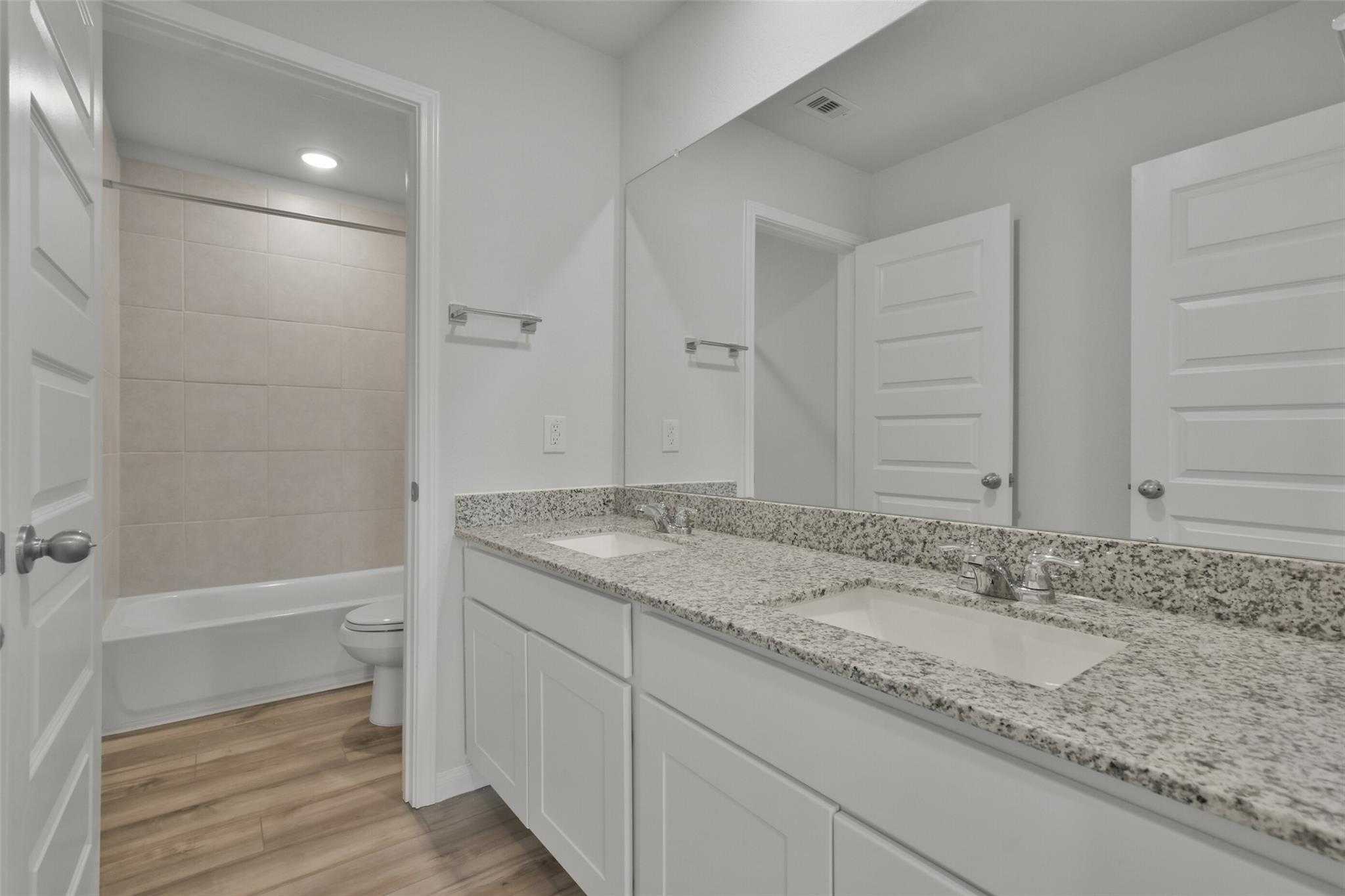 Modern master bathroom featuring double vanity with quartz countertops, soaking tub, and tiled walk-in shower in Davidson Homes The Tierra A, Dayton, Texas