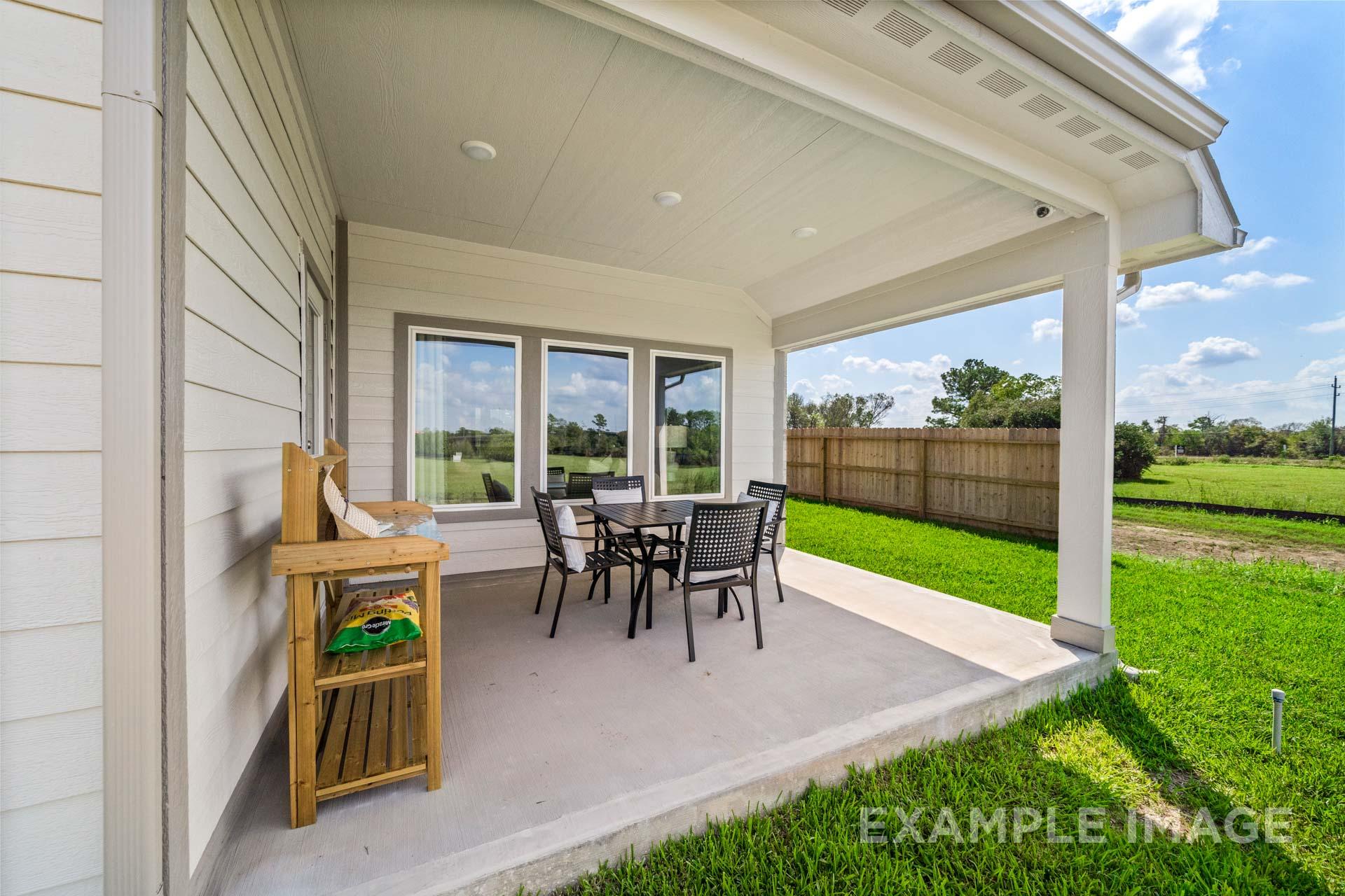 Covered patio of The Acadia A Davidson Homes design featuring outdoor dining set, wooden server, and lush green backyard in Magnolia, Texas