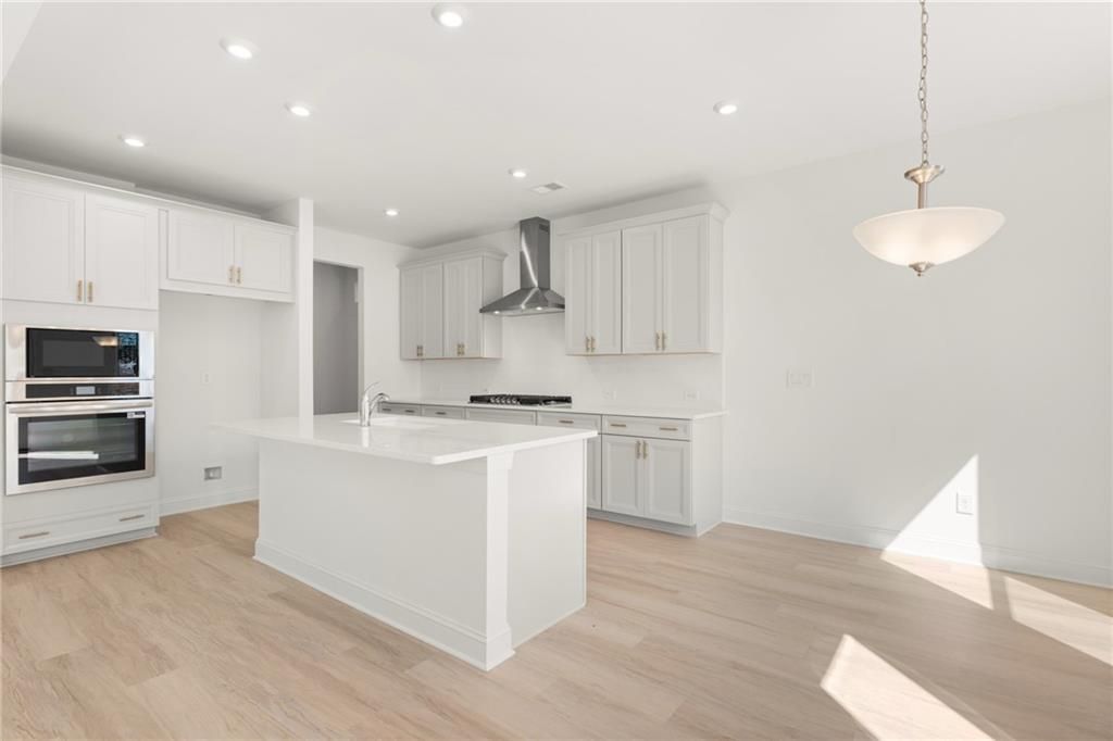 Modern white shaker kitchen with large quartz island, stainless double oven, gas range, and oak floors in Davidson Homes The Gavin E, Kennesaw, GA