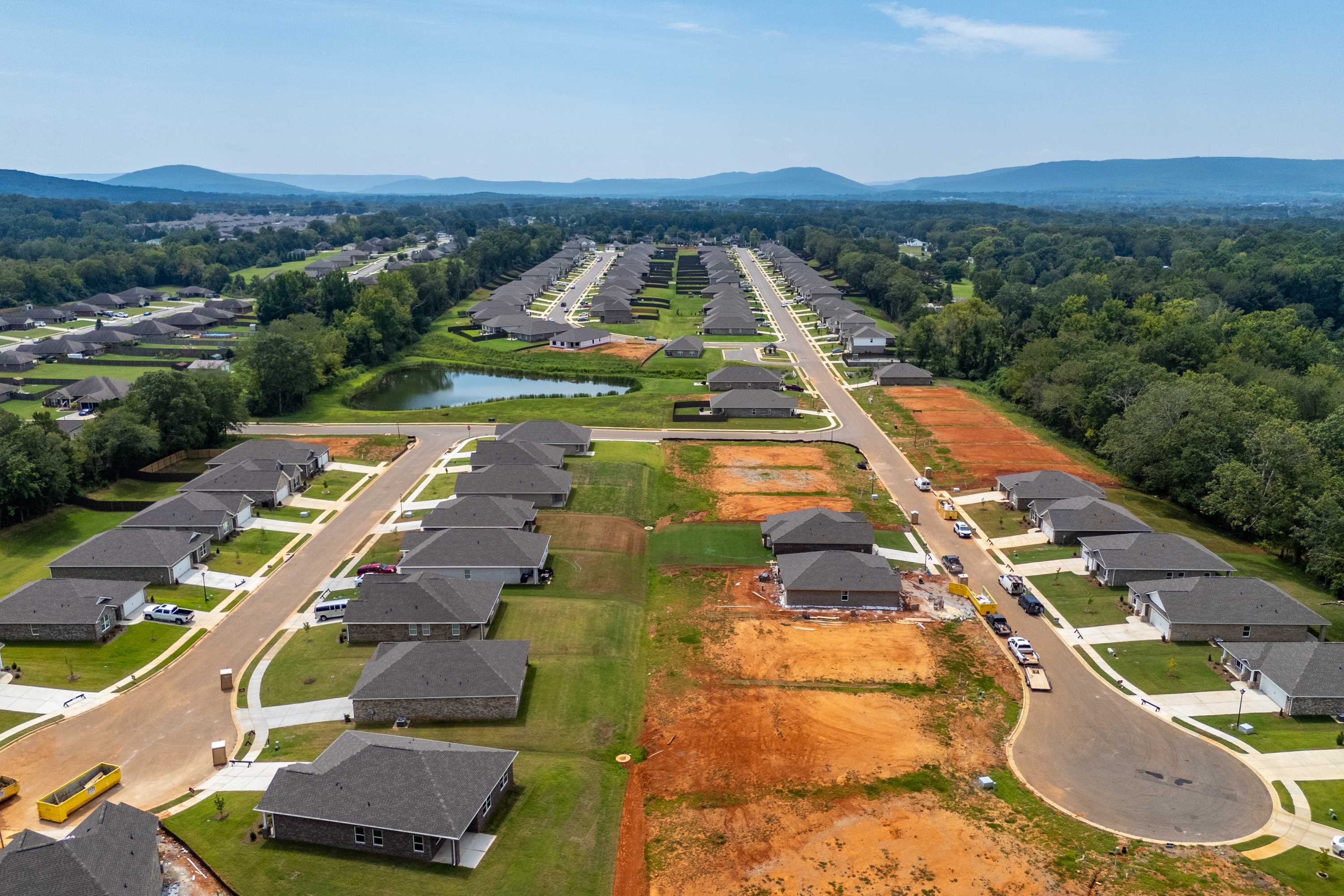 Aerial view of Flint Meadows neighborhood in New Market Alabama with new homes construction sites pond wooded areas and mountain backdrop