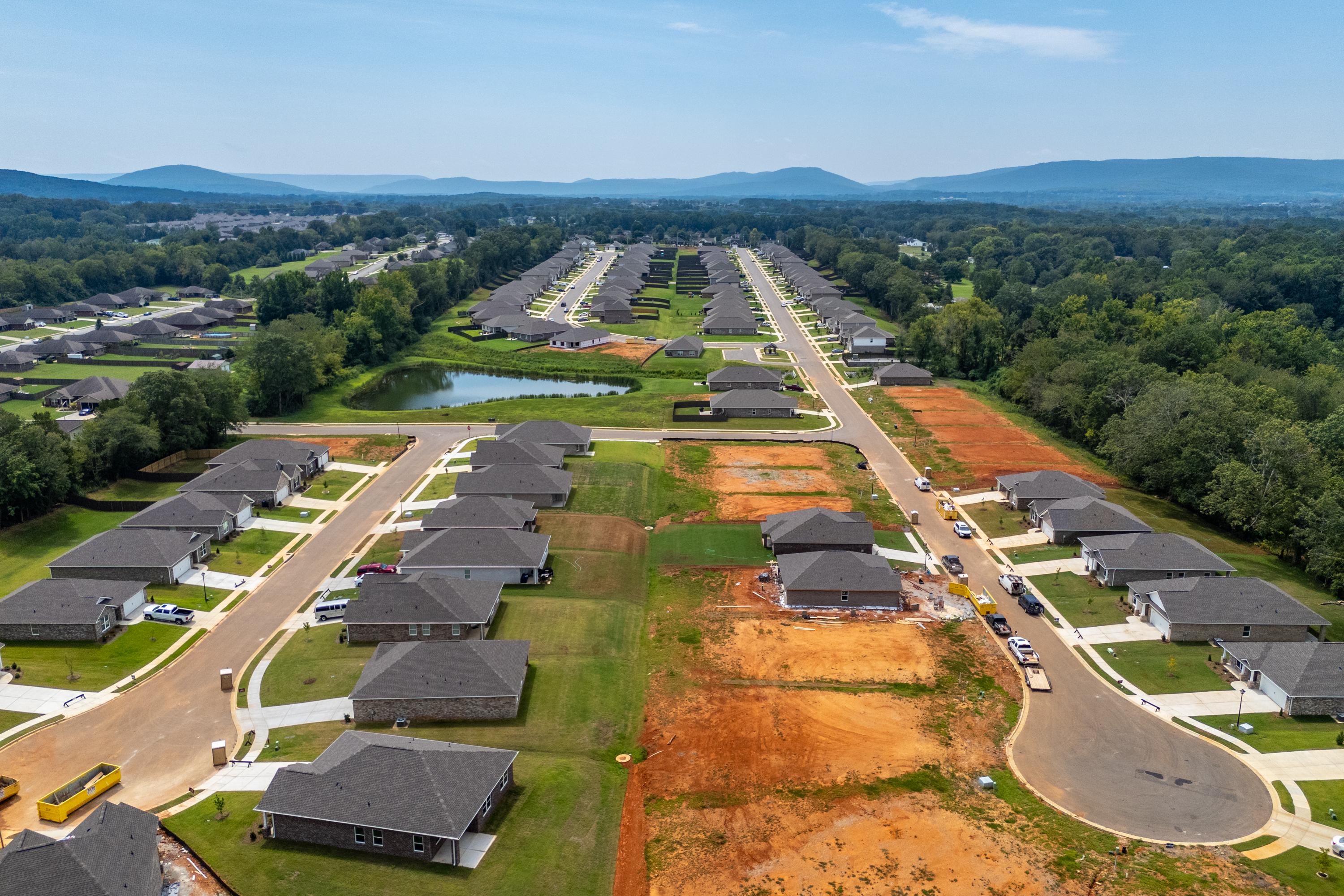 Aerial view of Flint Meadows neighborhood in New Market Alabama with new homes construction sites pond wooded areas and mountain backdrop