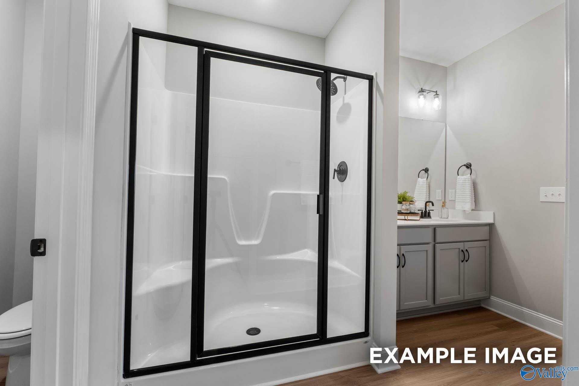 Modern bathroom with glass shower enclosure, white tiles, and gray vanity in Davidson Homes The Daphne C, Owens Cross Roads, Alabama