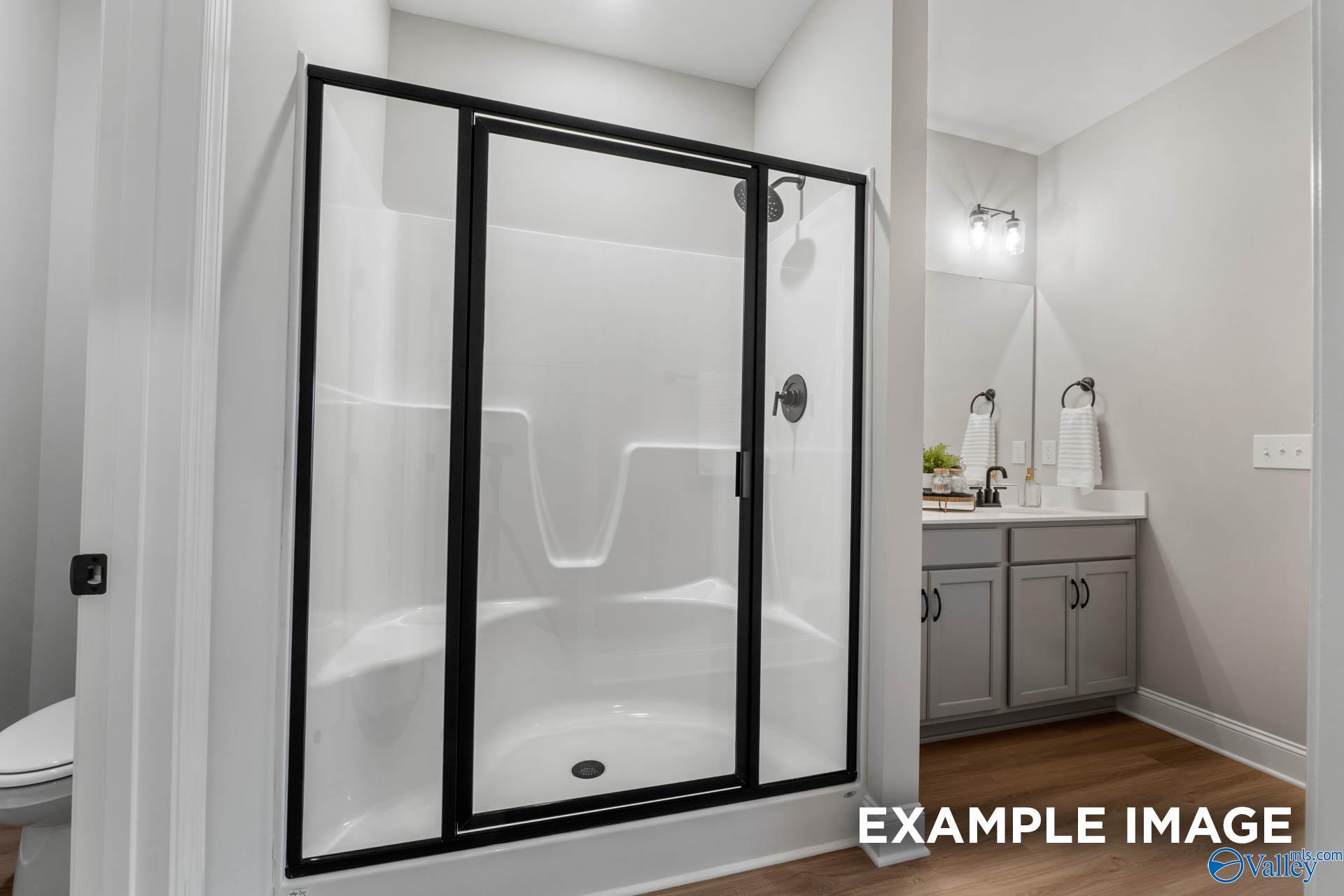 Modern bathroom with glass shower enclosure, white tiles, and gray vanity in Davidson Homes The Daphne C, Owens Cross Roads, Alabama