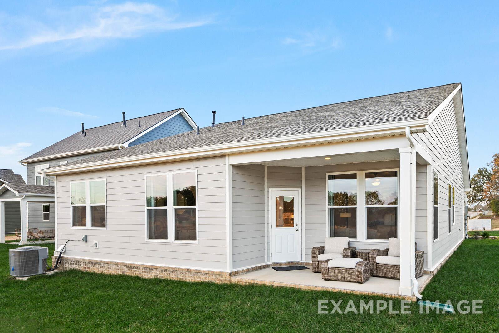 Rear elevation of The Franklin B single-story home with covered porch, large windows, wicker seating, and lush green yard in White House, TN