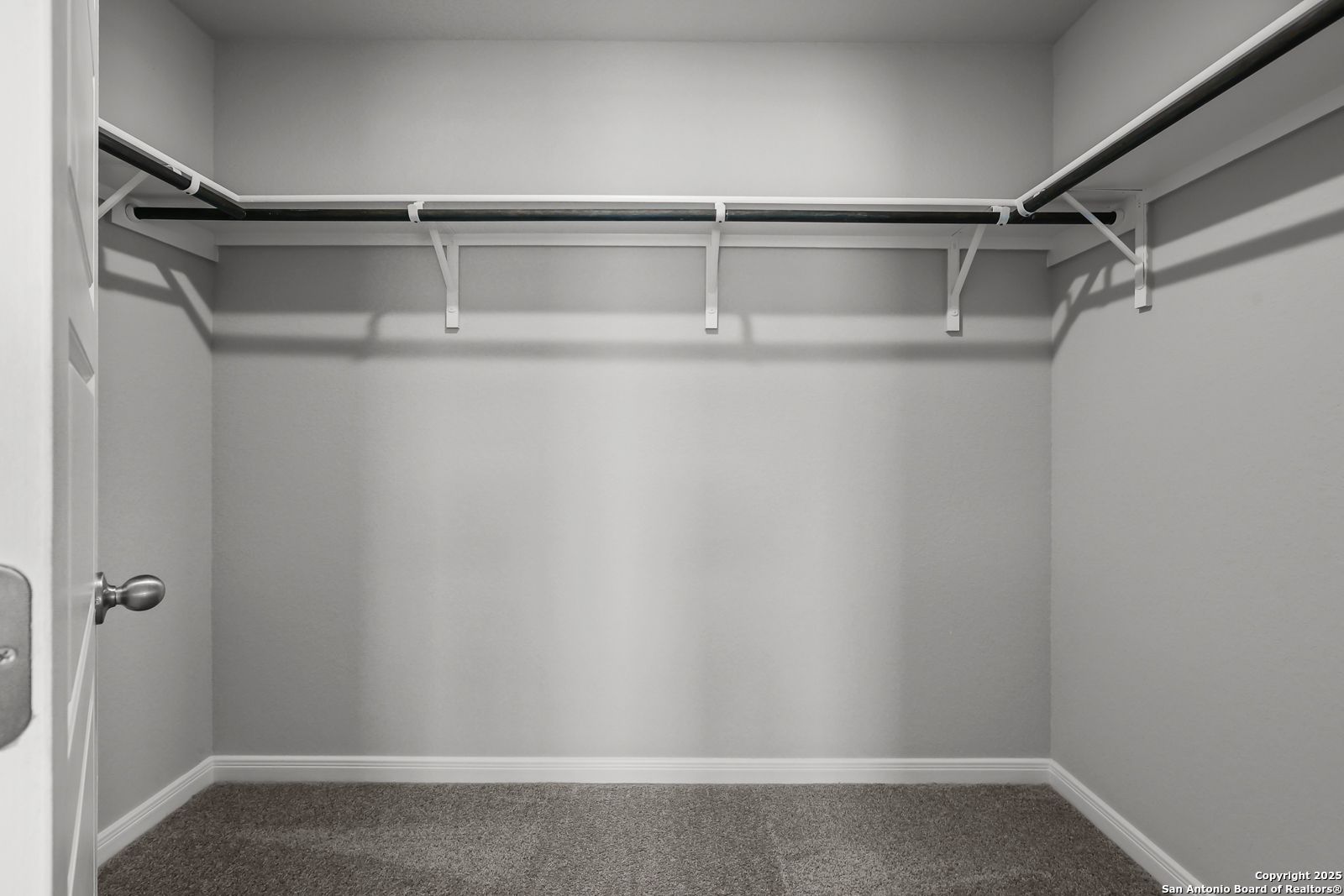 Spacious walk-in closet with white rods and gray carpet in master suite of Davidson Homes The Gillian C in San Antonio, Texas