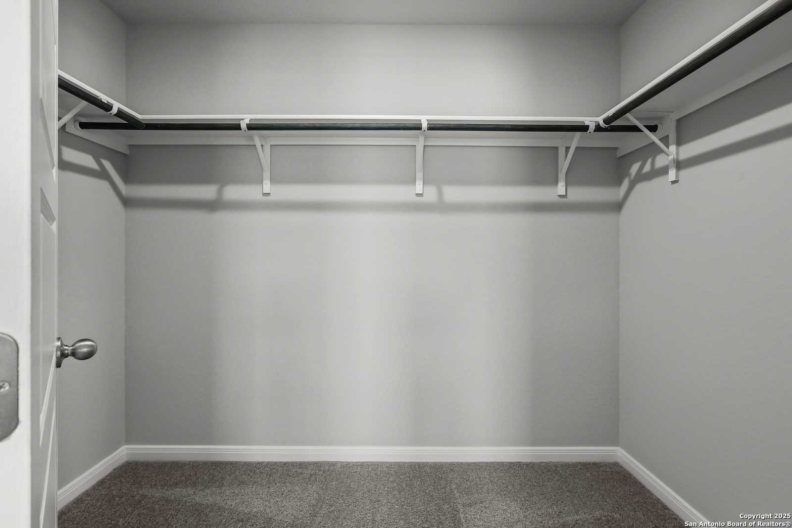 Spacious walk-in closet with white rods and gray carpet in master suite of Davidson Homes The Gillian C in San Antonio, Texas