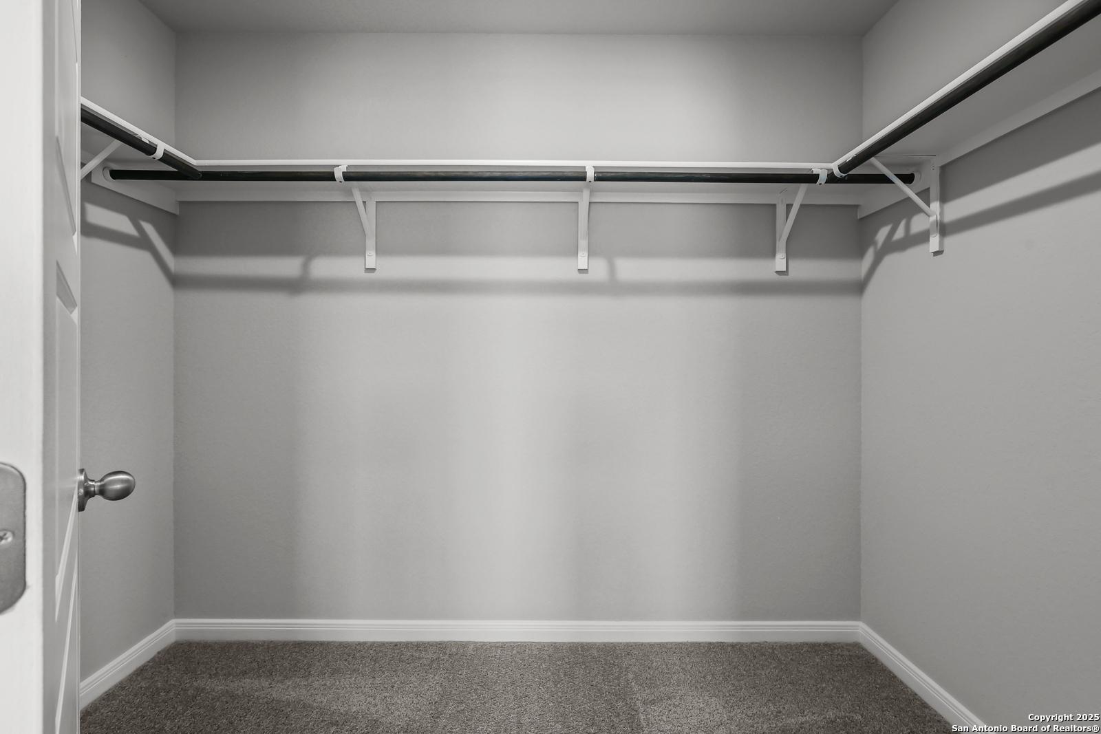Spacious walk-in closet with white rods and gray carpet in master suite of Davidson Homes The Gillian C in San Antonio, Texas