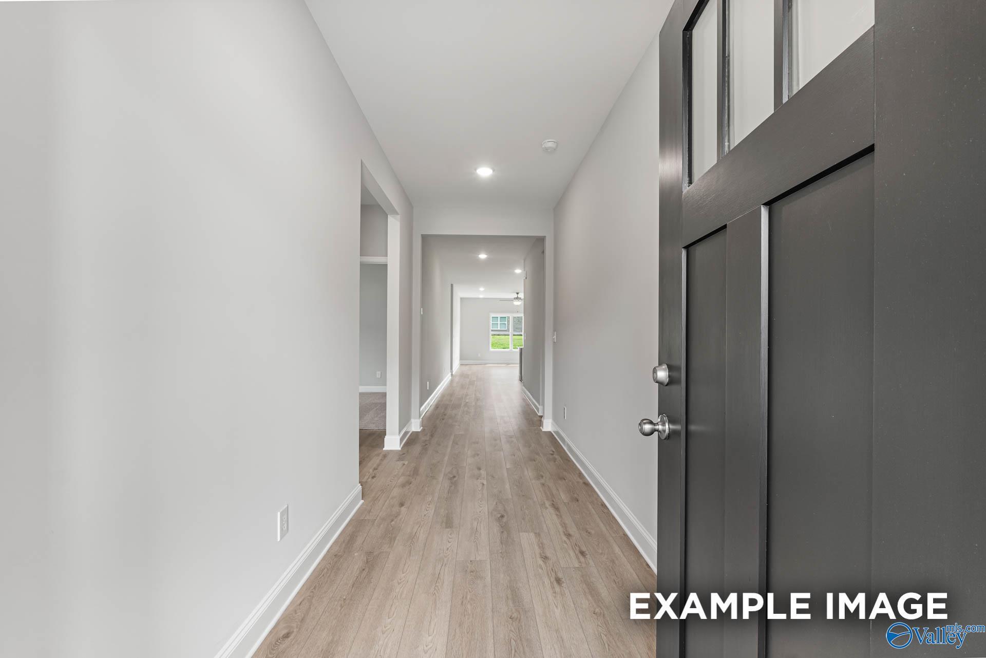 Spacious entry hallway with light oak floors, white walls, and dark front door in The Daphne 4-bedroom home, Hazel Green, Alabama