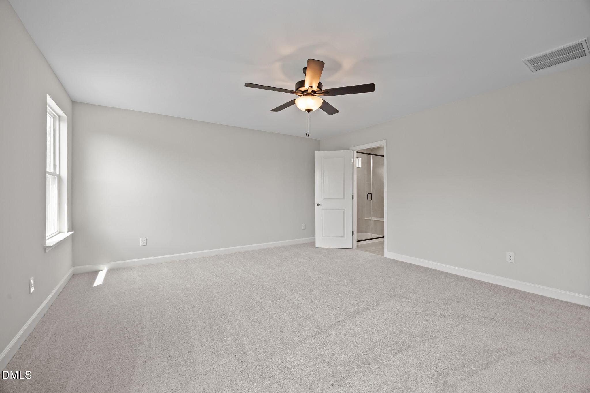 Bright bedroom with ceiling fan, neutral gray walls, carpeted floor, and en-suite bath in Davidson Homes The Willow D, Wendell, NC