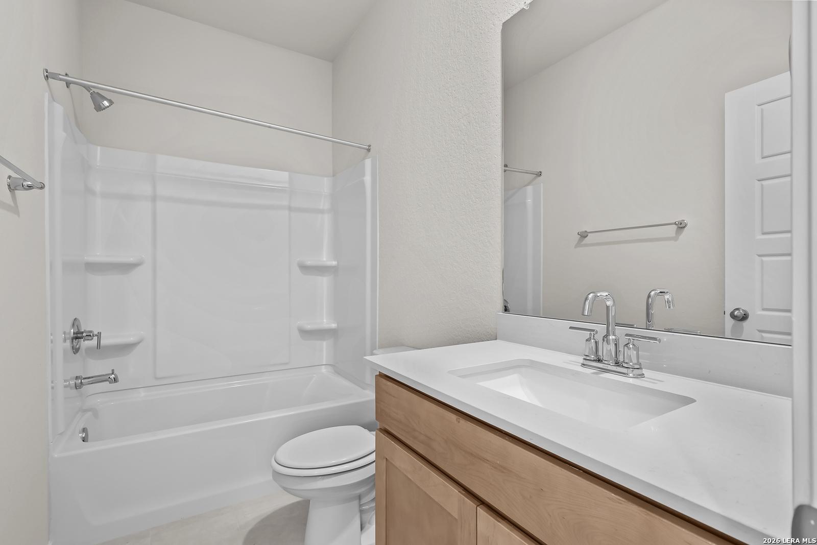 Modern bathroom with shower-tub combo and wood vanity in The Gillian B floor plan at Meadows at Oak Creek, San Antonio.