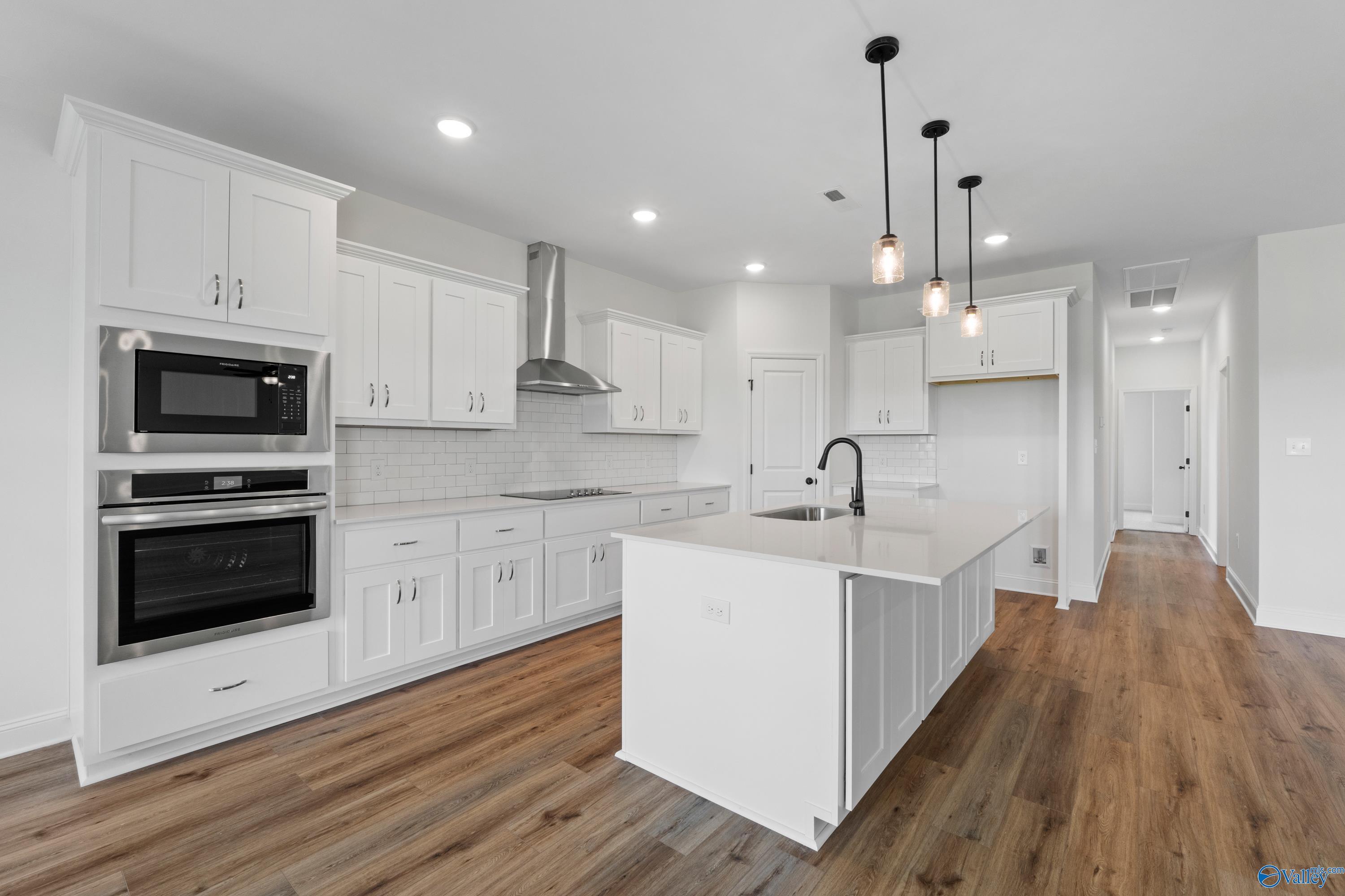 Modern white kitchen with large island, stainless double oven, pendant lights, and hardwood floors in Davidson Homes The Rockford B, Toney, Alabama