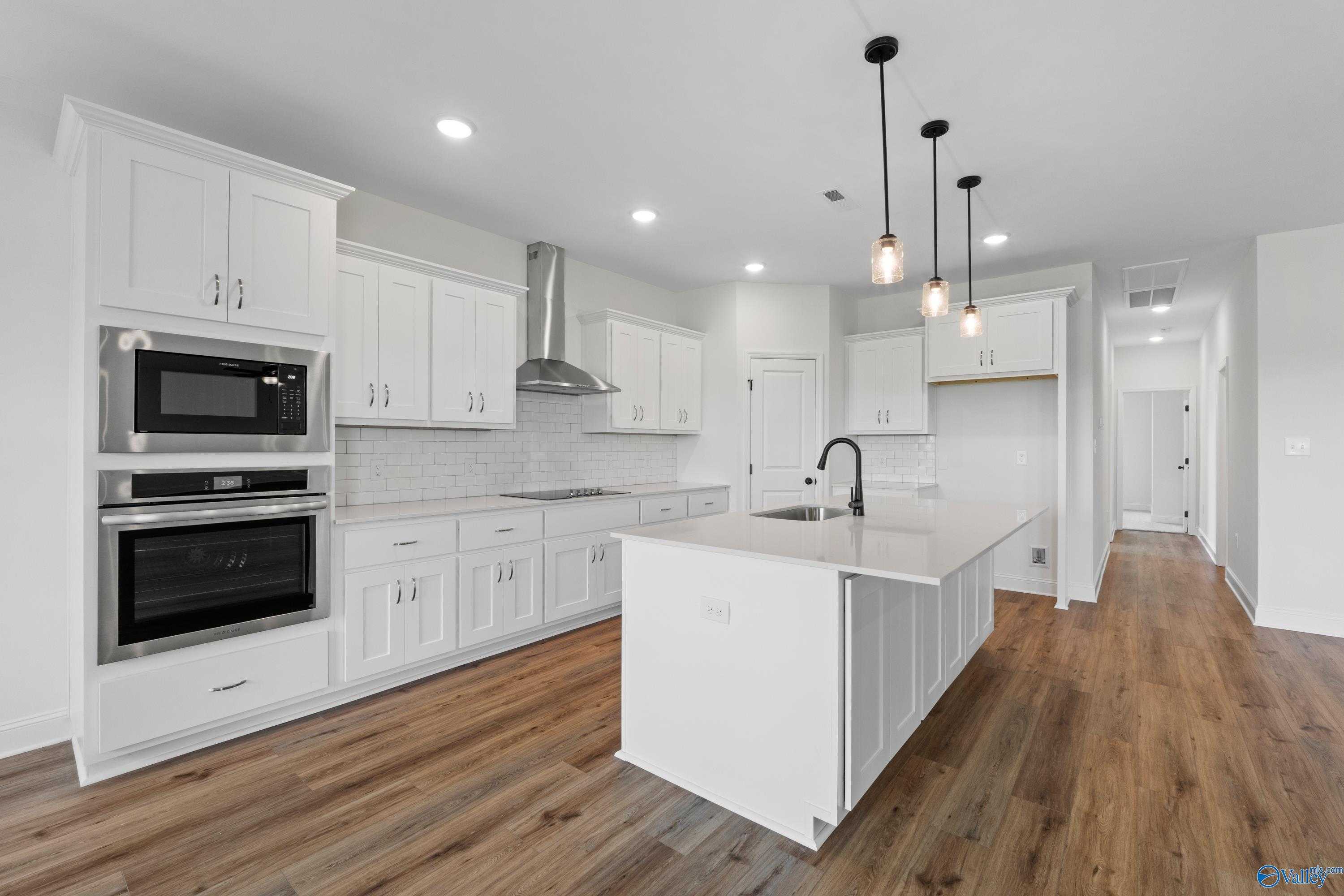 Modern white kitchen with large island, stainless steel double oven, subway tile backsplash, and pendant lights in The Rockford B, Toney, Alabama