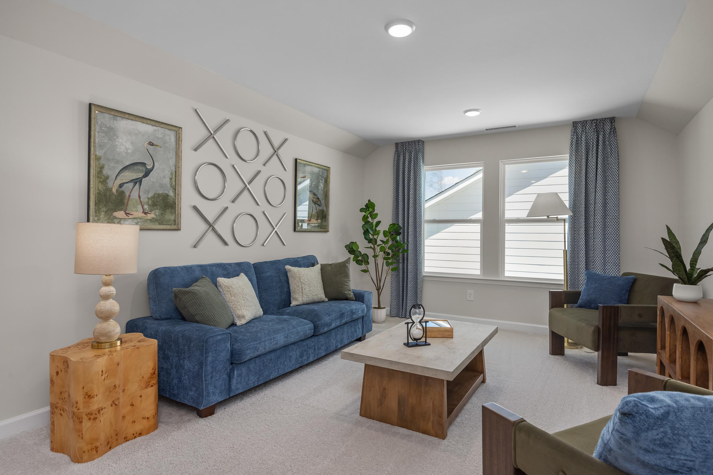 Cozy living room at Sage on North Main in Wake Forest NC featuring blue velvet sofa, XOXO wall decor, plants and neutral tones