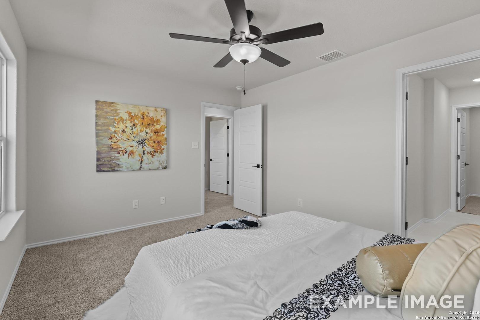 Cozy bedroom with ceiling fan, white bed in neutral linens, yellow tree wall art in Davidson Homes The Trinity B, San Antonio