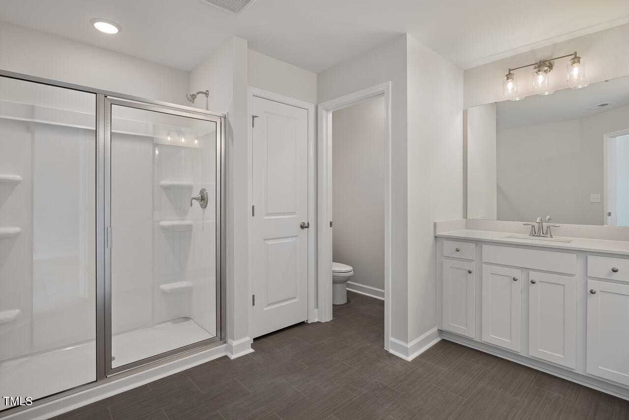 Modern master bathroom with glass walk-in shower, white double vanity, mirror, and toilet in Davidson Homes The Graham, Fuquay-Varina, NC