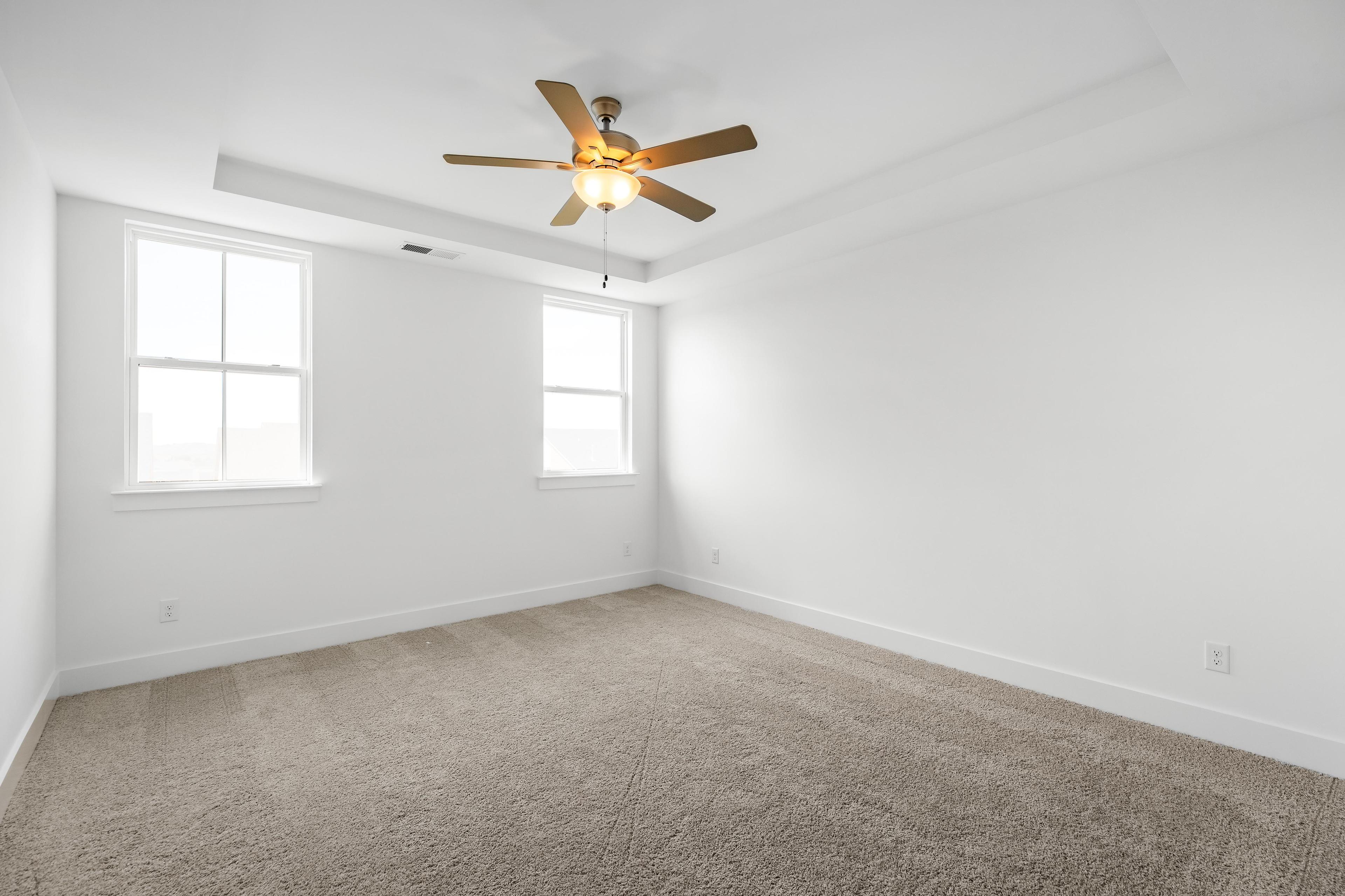 Spacious bedroom in The Cedar D featuring neutral carpet, white walls, and a tray ceiling with a modern ceiling fan.