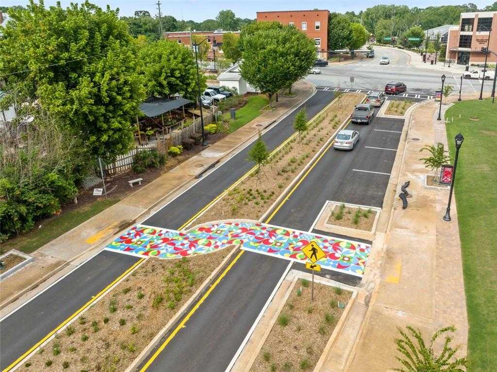 Vibrant rainbow pedestrian crosswalk at Hoschton intersection, lined with trees and brick buildings in Wehunt Meadows, Georgia