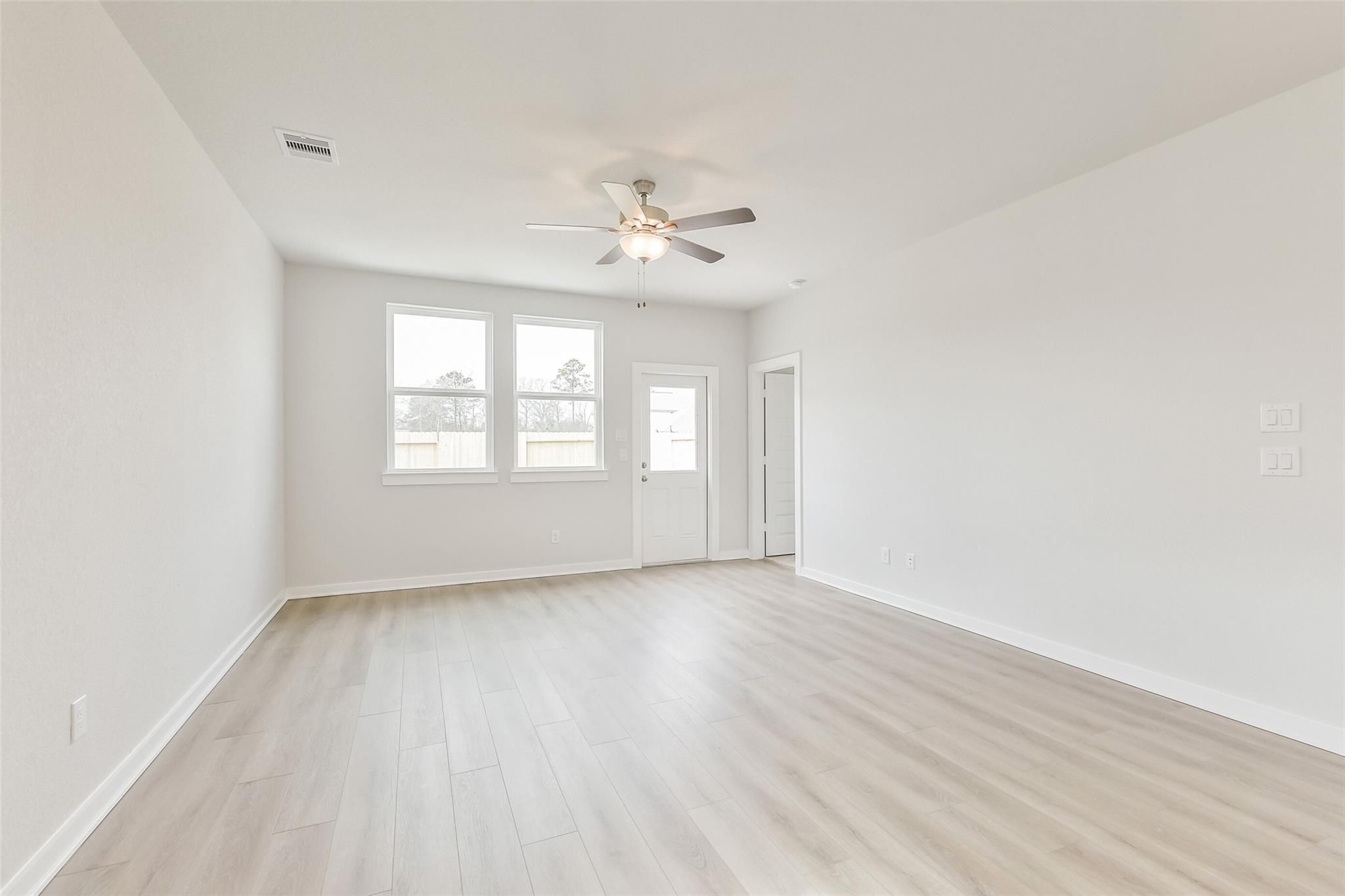 Spacious living room with large windows, ceiling fan, and light wood flooring in Davidson Homes The Frio G, Cleveland TX