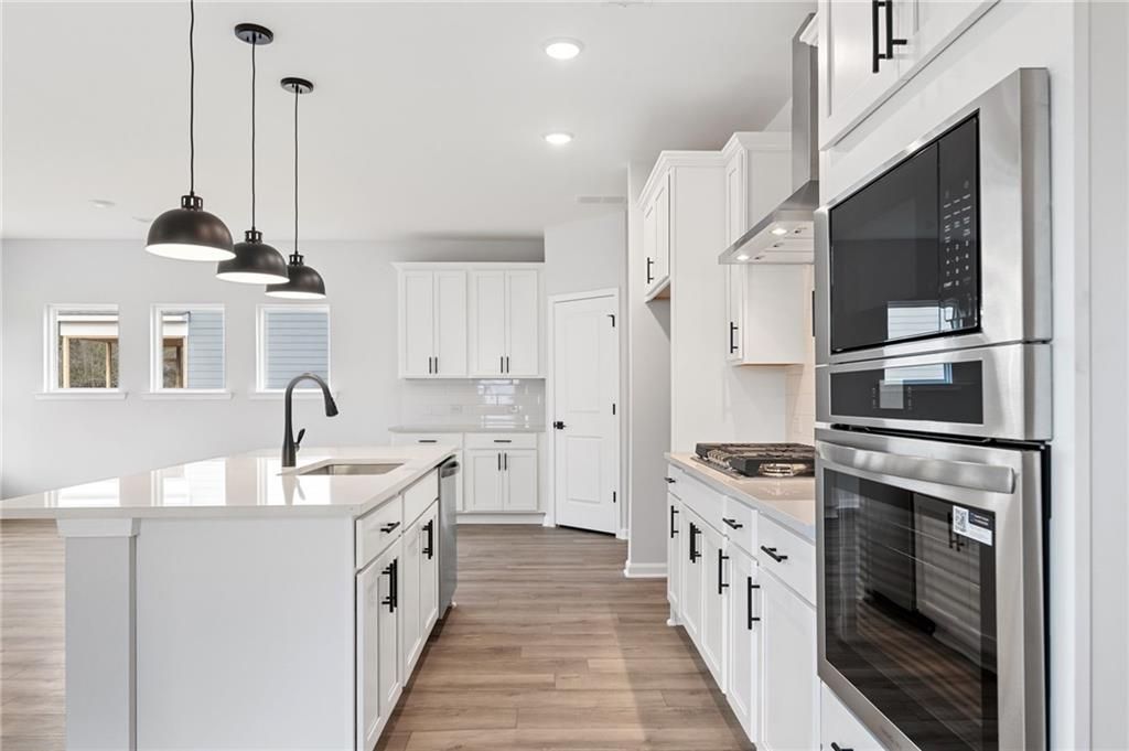 Modern white kitchen with quartz island, stainless steel oven and microwave, pendant lights in Davidson Homes The Rabun C, Winder, Georgia