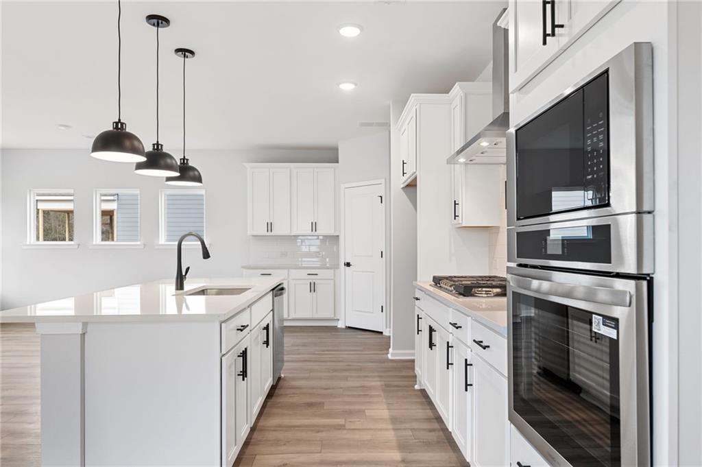 Modern white kitchen with quartz island, stainless steel oven and microwave, pendant lights in Davidson Homes The Rabun C, Winder, Georgia