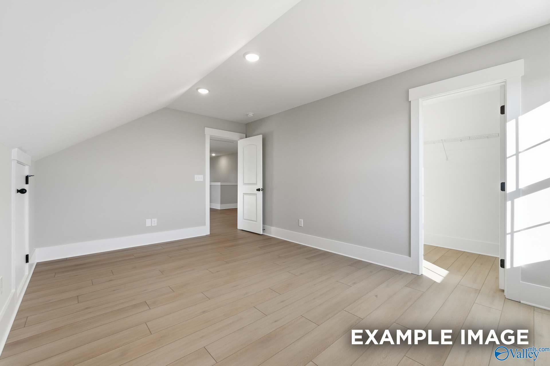 Bright upstairs bedroom with vaulted ceiling, hardwood floors, walk-in closet, and bathroom in Davidson Homes The Emory, Decatur, Alabama