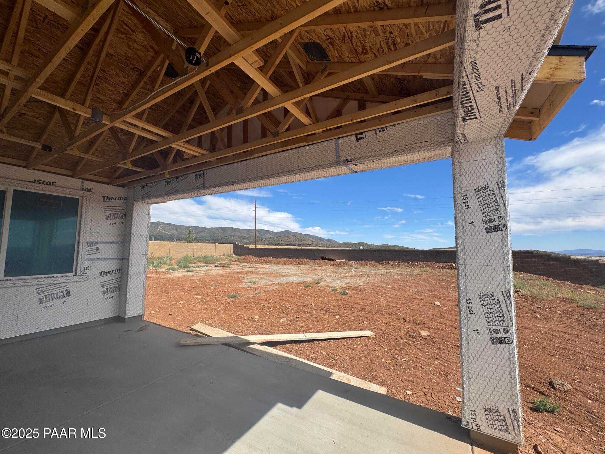 Framed single-story home with wooden trusses, house wrap walls, and expansive garage opening amid desert landscape in Prescott Valley, Arizona - Evermore Homes The Sunrise A
