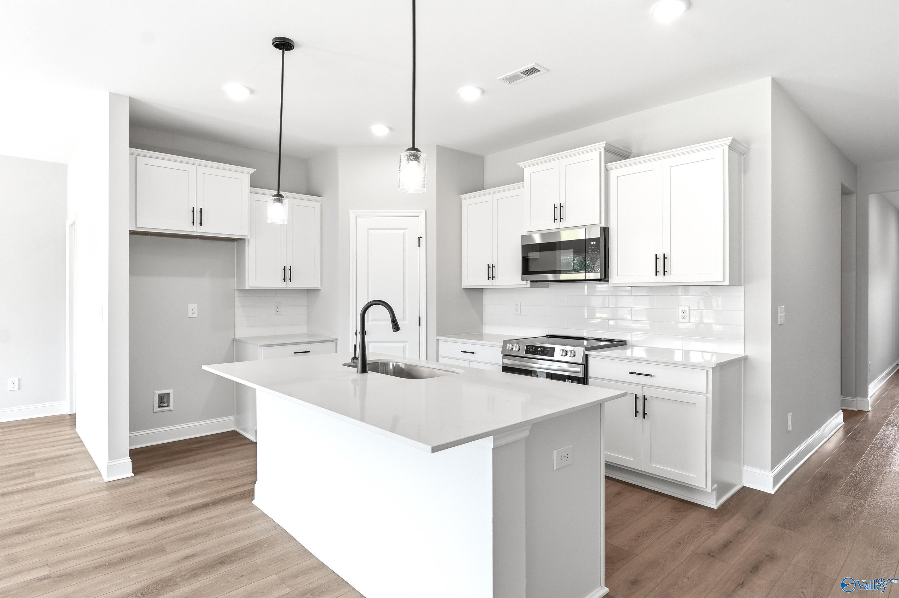 Modern kitchen with white cabinets, quartz island, and stainless appliances in The Daphne C home at Flint Meadows, Alabama.