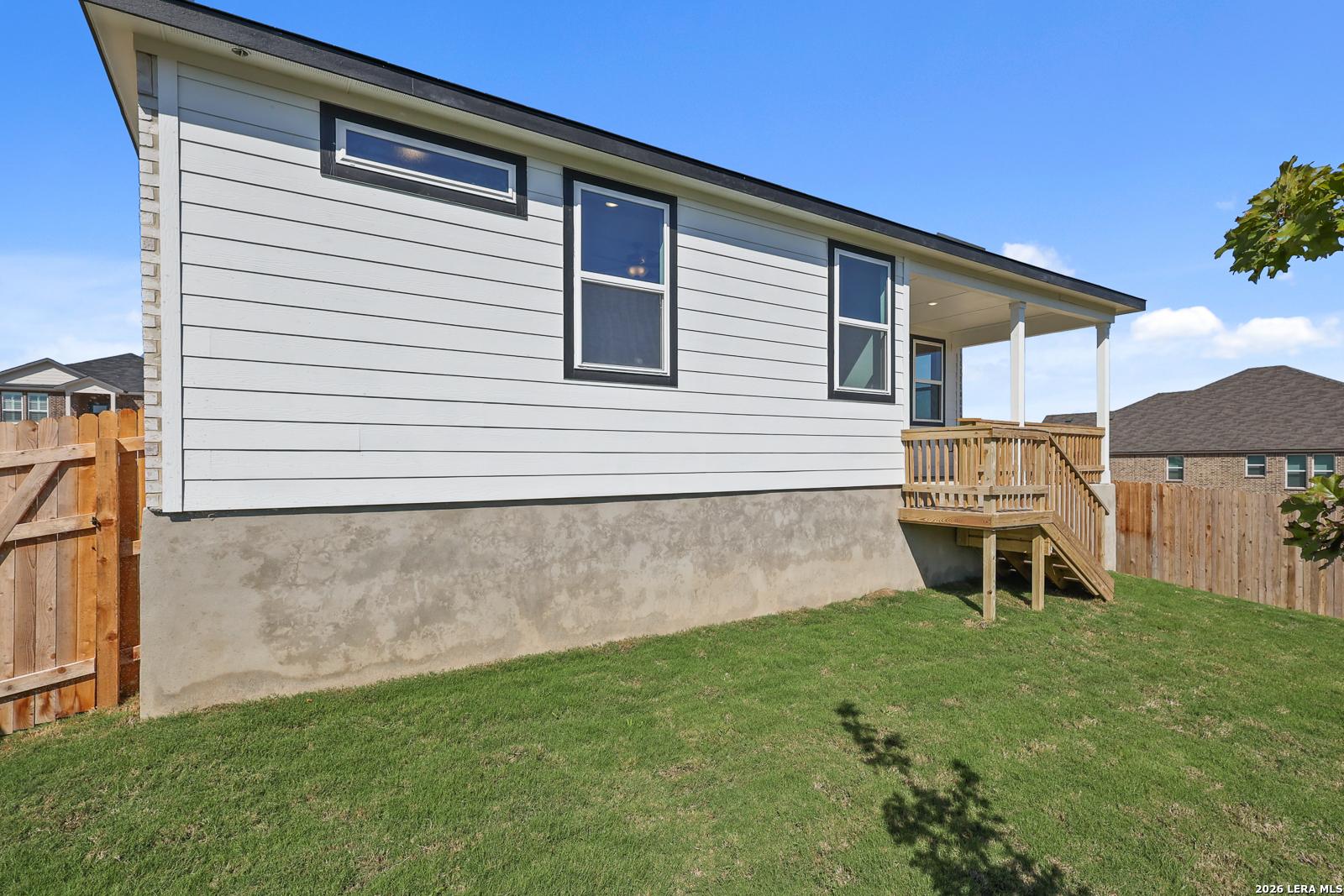 White single-story home exterior with covered back patio, wooden deck stairs, and fenced backyard in Comanche Ridge, San Antonio, Texas