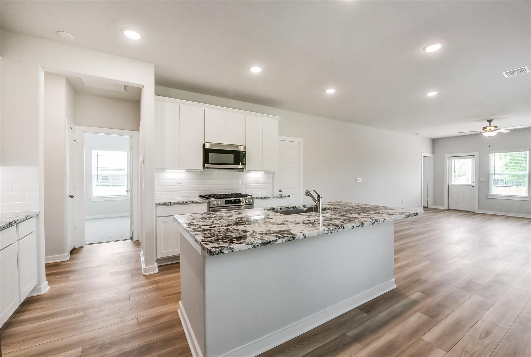 Open-concept kitchen with white cabinets, gray granite island, stainless appliances in The Frio G by Davidson Homes, Magnolia TX