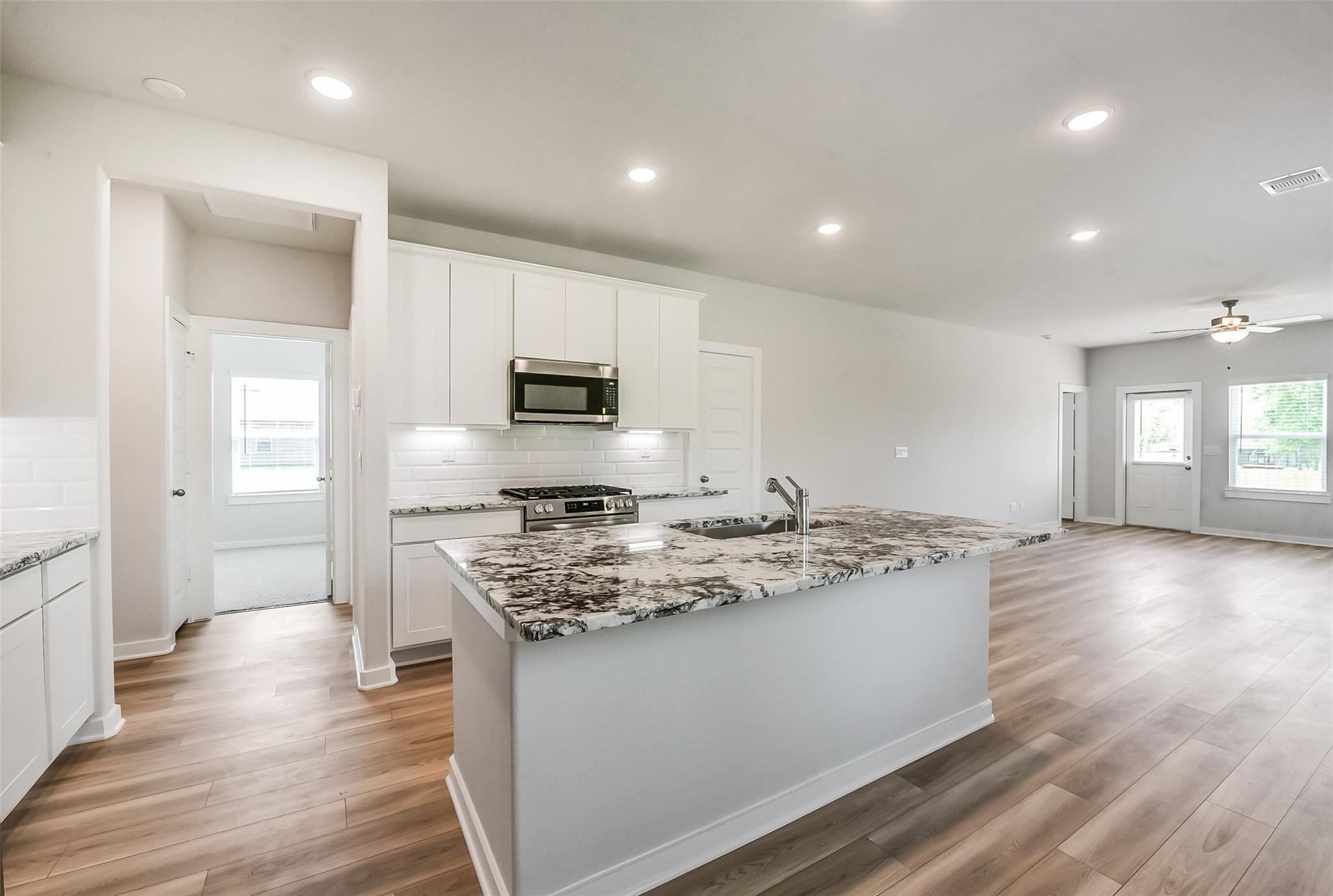 Open-concept kitchen with white cabinets, gray granite island, stainless appliances in The Frio G by Davidson Homes, Magnolia TX