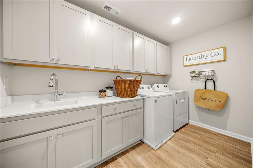 Modern laundry room featuring white shaker cabinets, deep sink, washer-dryer set in Davidson Homes The Willow B, Riverwood, Dallas, Georgia