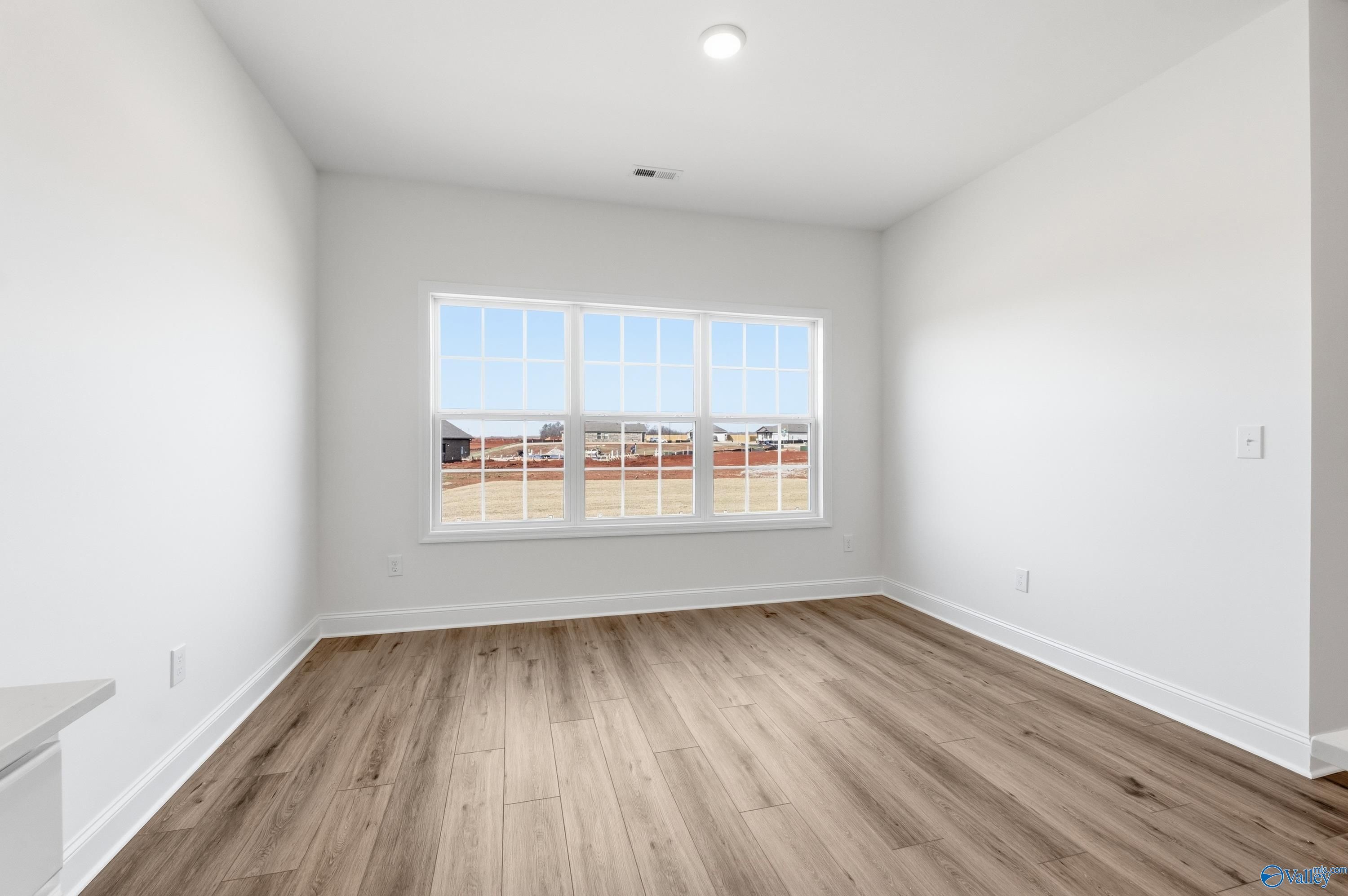 Bright secondary bedroom with large window view of new homes, light wood floors in Davidson Homes Montgomery C, Harvest AL
