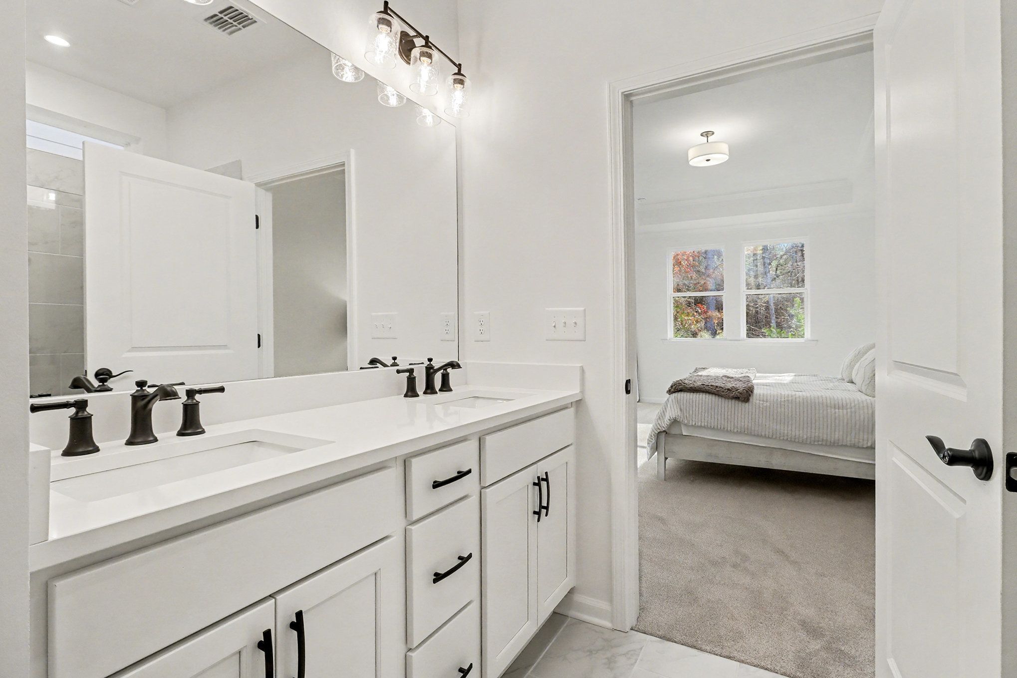 Modern master bathroom featuring double vanity with black faucets, large mirror, and glass shower in Davidson Homes The Daphne B, Loganville, GA