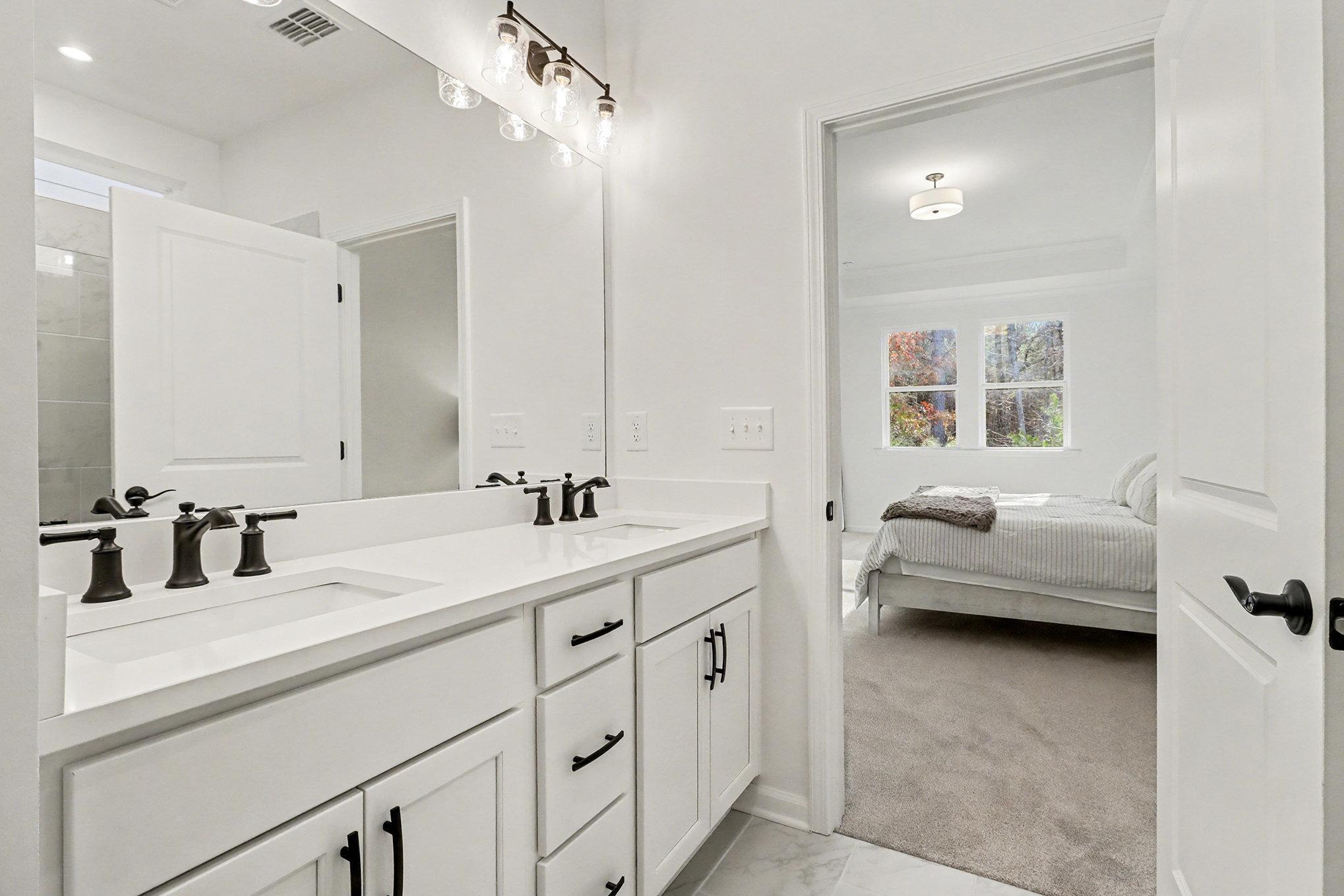 Modern master bathroom featuring double vanity with black faucets, large mirror, and glass shower in Davidson Homes The Daphne B, Loganville, GA