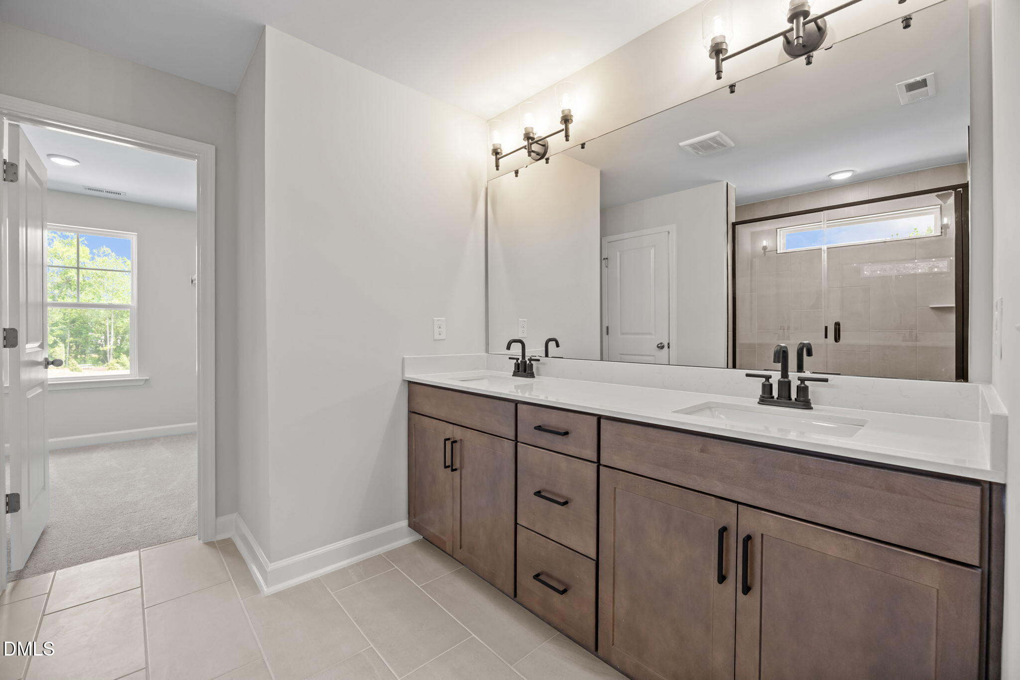 Modern master bathroom featuring double vanity with quartz countertop, dark cabinets, and glass shower in The Willow D by Davidson Homes, Wendell, NC