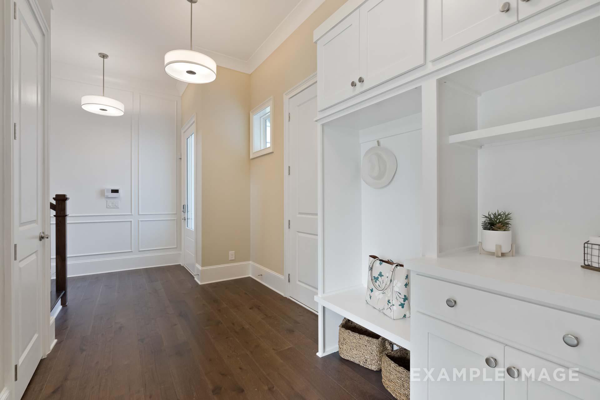 Spacious mudroom in The Seaside C with white cabinetry, built-in bench, storage hooks, baskets, and hardwood floors