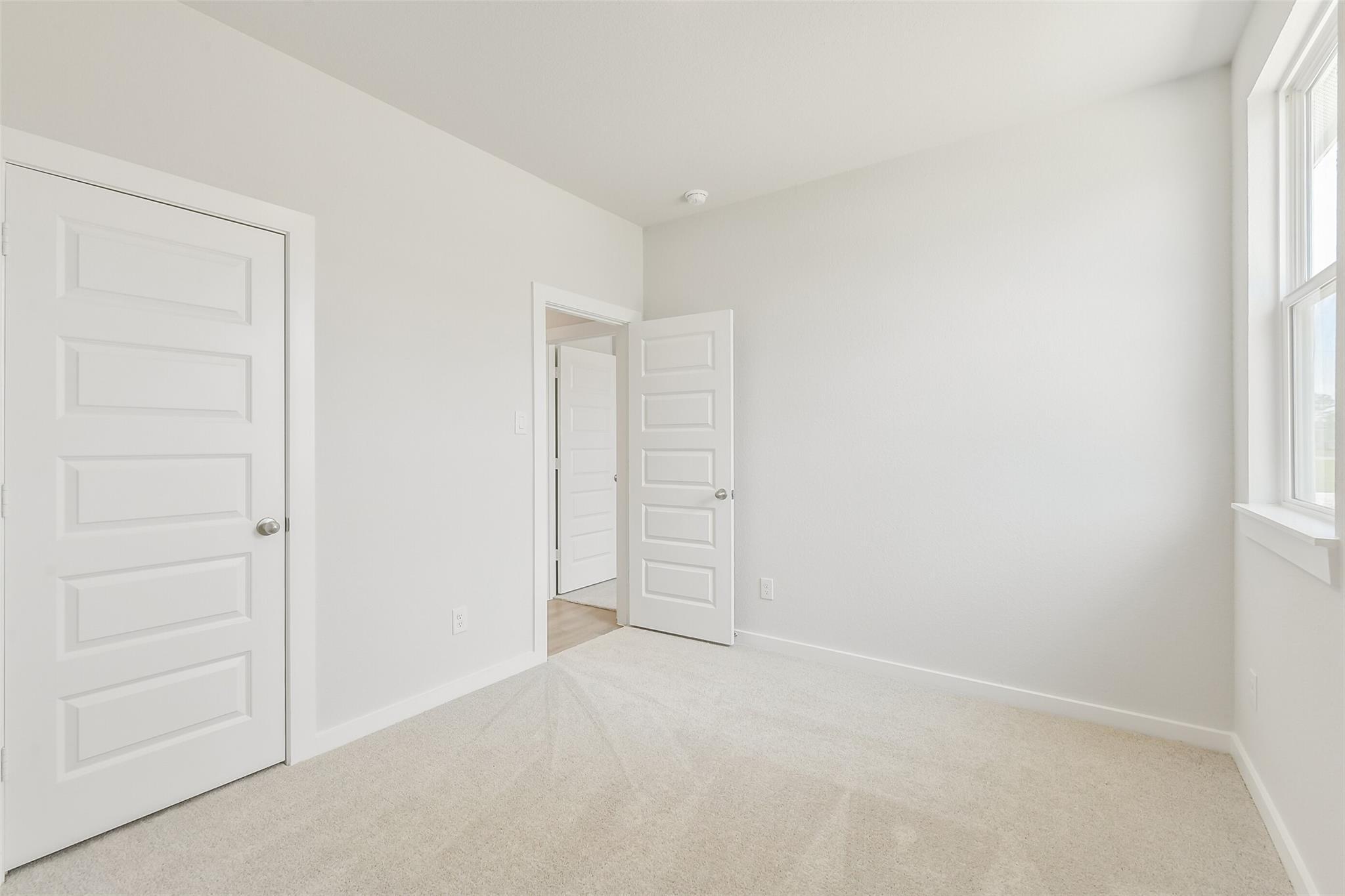 Bright secondary bedroom with beige carpet, white paneled doors to bath, window in The Frio G home, Conroe Texas