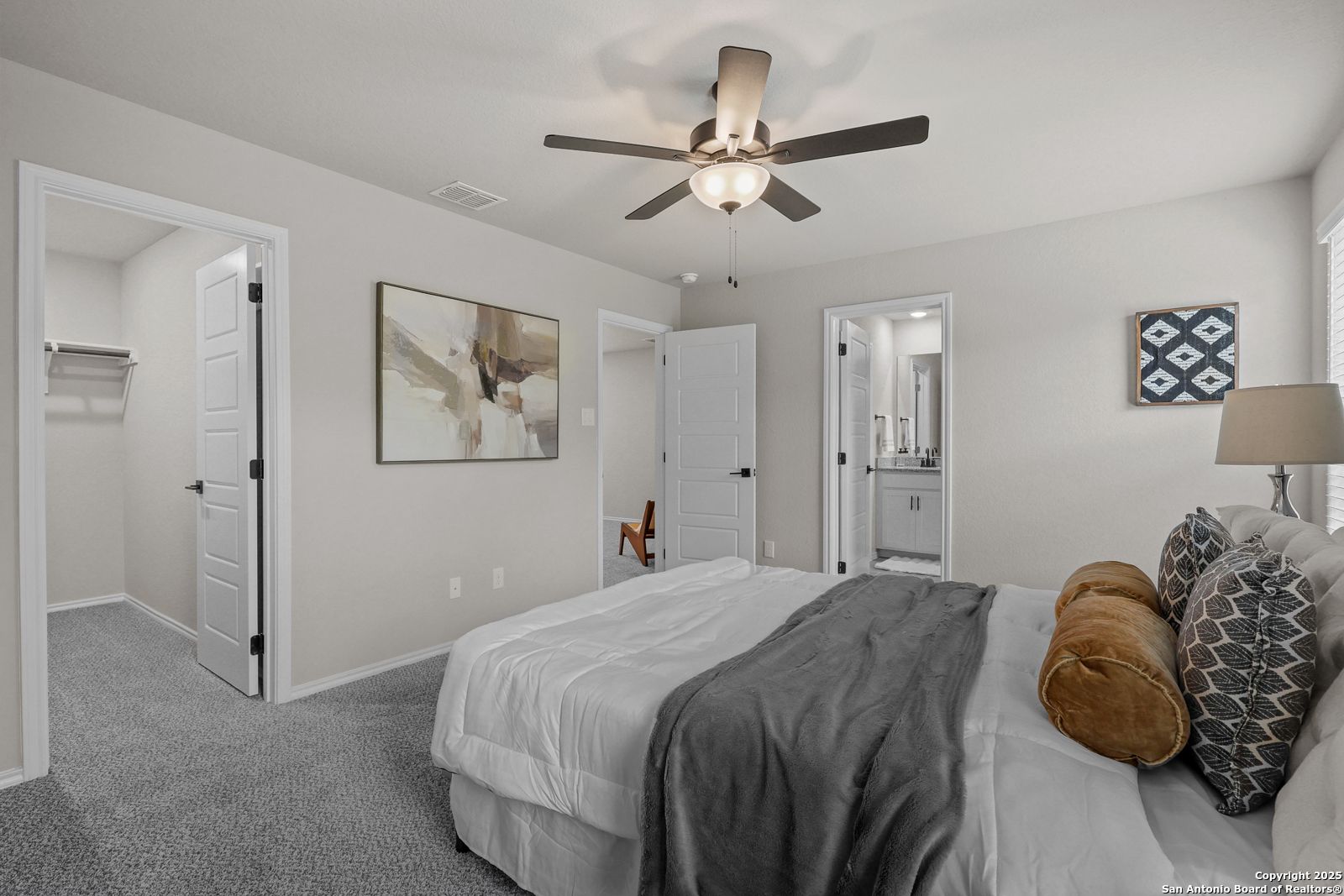 Spacious master bedroom with plush bed, ceiling fan, abstract art, walk-in closet, and en-suite bath in Davidson Homes The Charlotte B, San Antonio, Texas