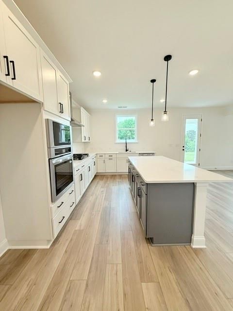 Modern kitchen with gray island, white cabinets, and stainless appliances in The Hickory B home at Wehunt Meadows, Hoschton.