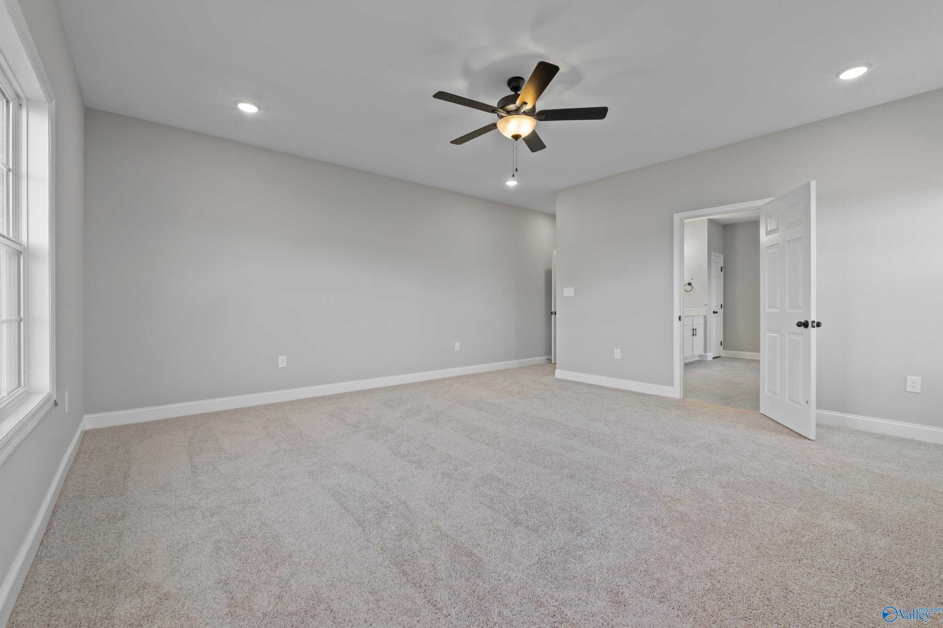 Spacious bedroom with ceiling fan, gray walls, and open door to en-suite bath in Davidson Homes The Valencia, Meridianville, AL