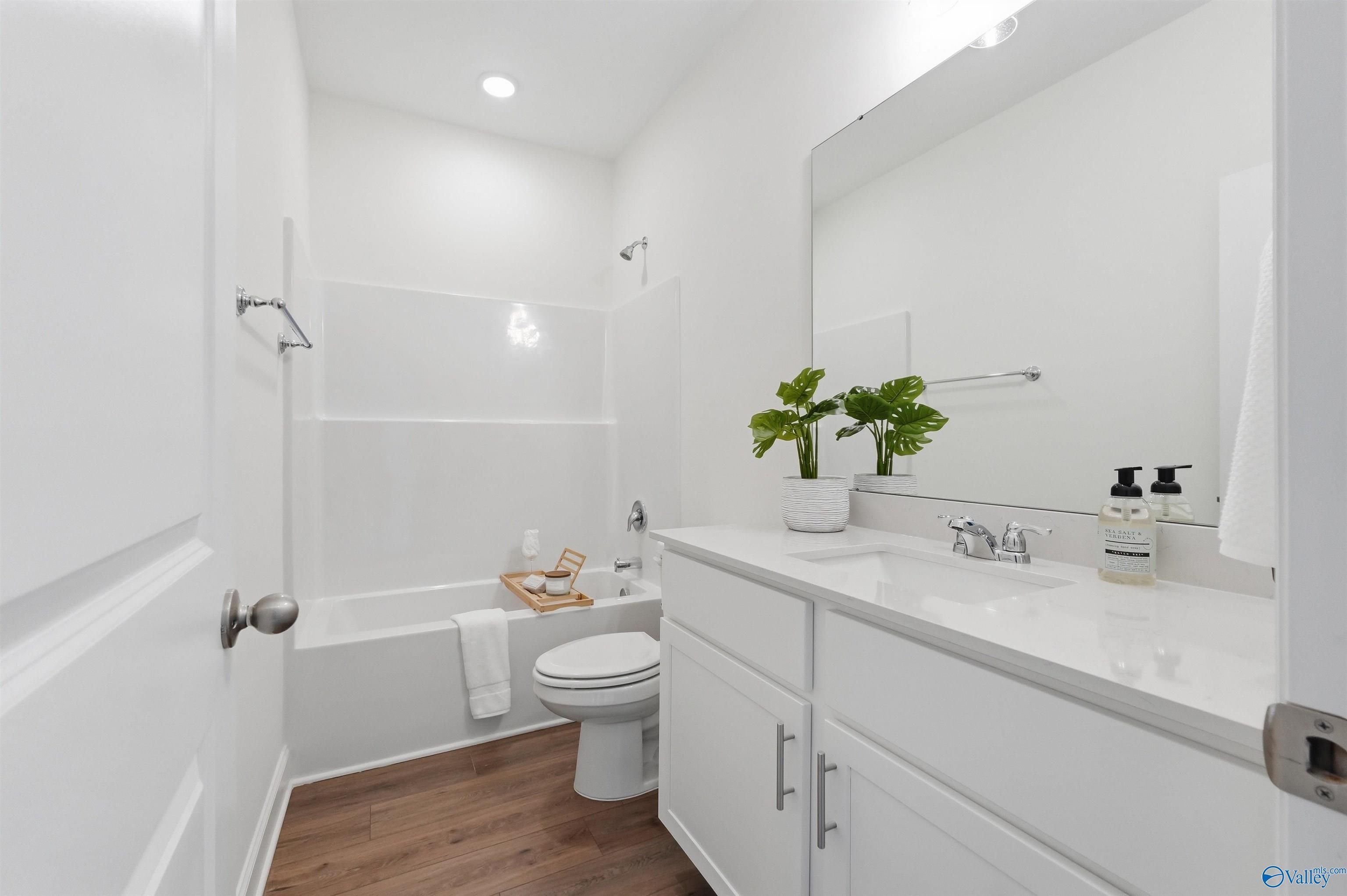 Modern bathroom with white vanity, tub-shower combo, and wood-look flooring in The Franklin C home at Lynn Meadows.