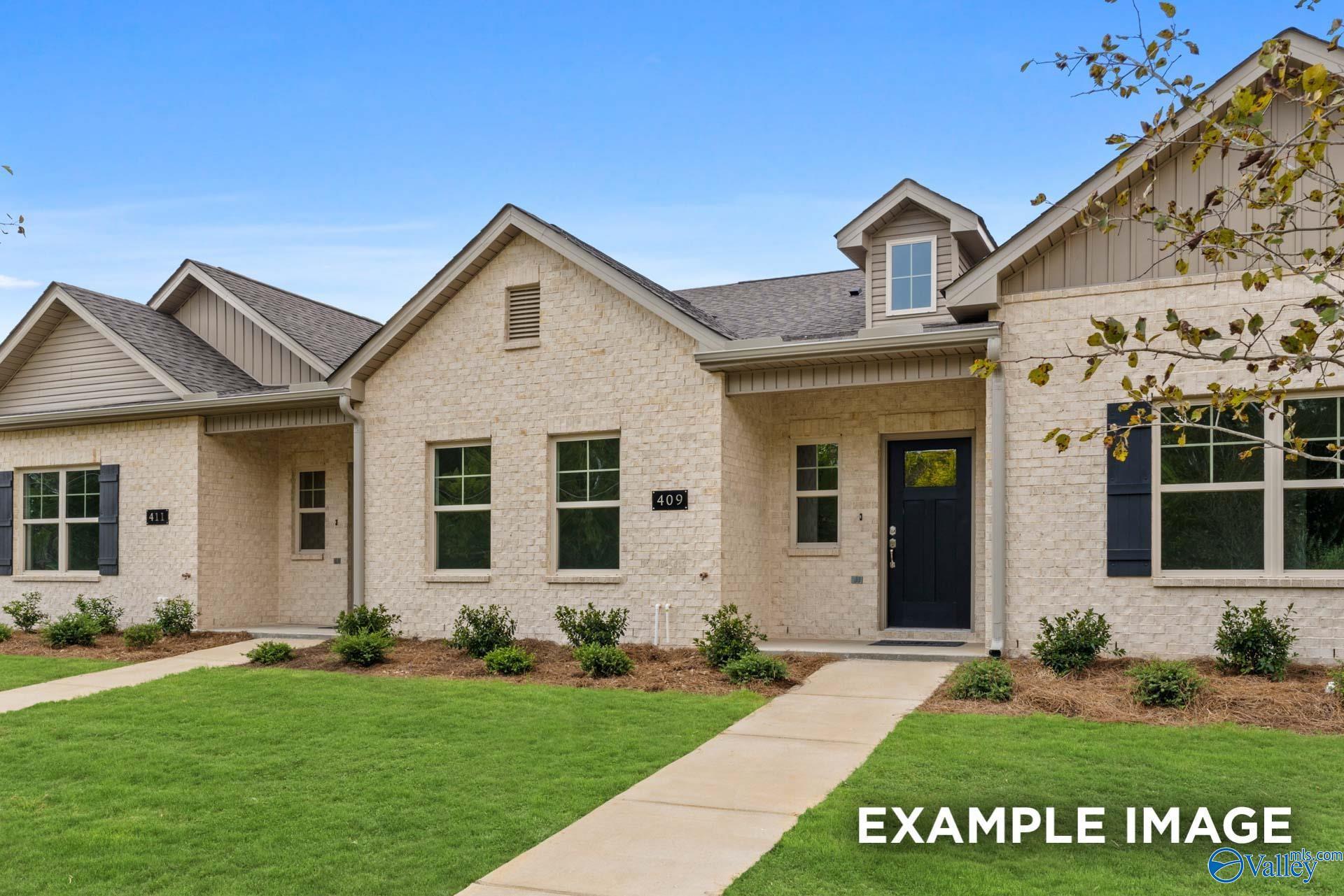 Beige brick single-story home with gabled roof, dark front door, and lush lawn in The Retreat at Cain Park, Hartselle, Alabama