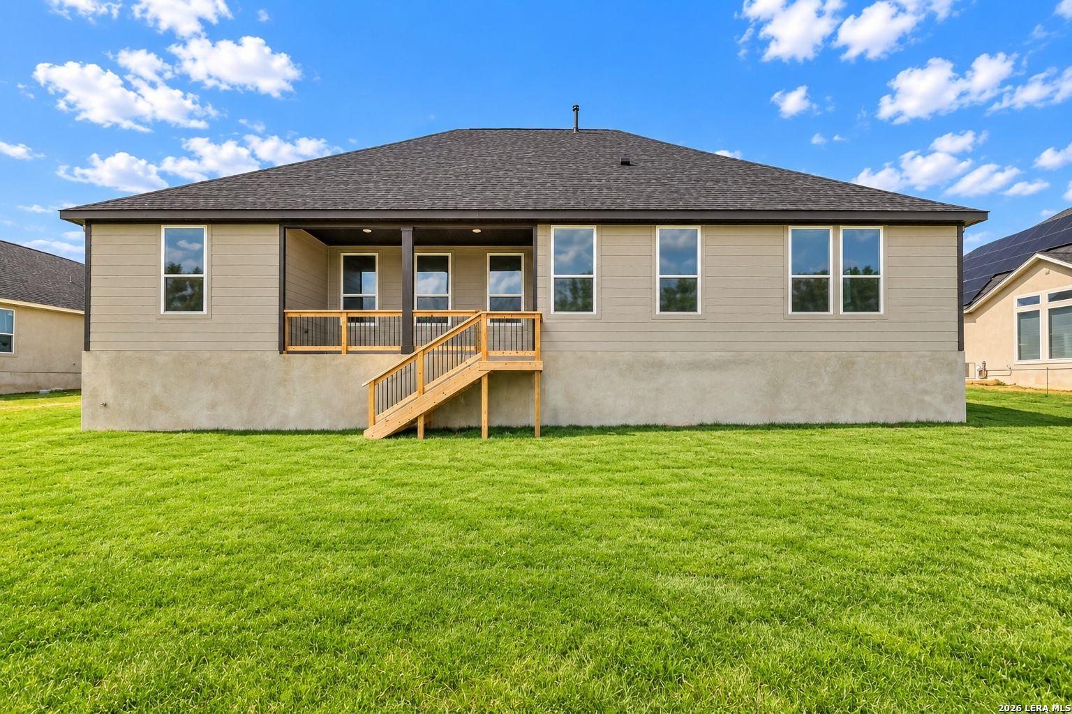 Rear exterior of Davidson Homes The Foster E single-story home with covered patio, wooden deck stairs, and spacious fenced backyard in Potranco Oaks, Castroville, Texas