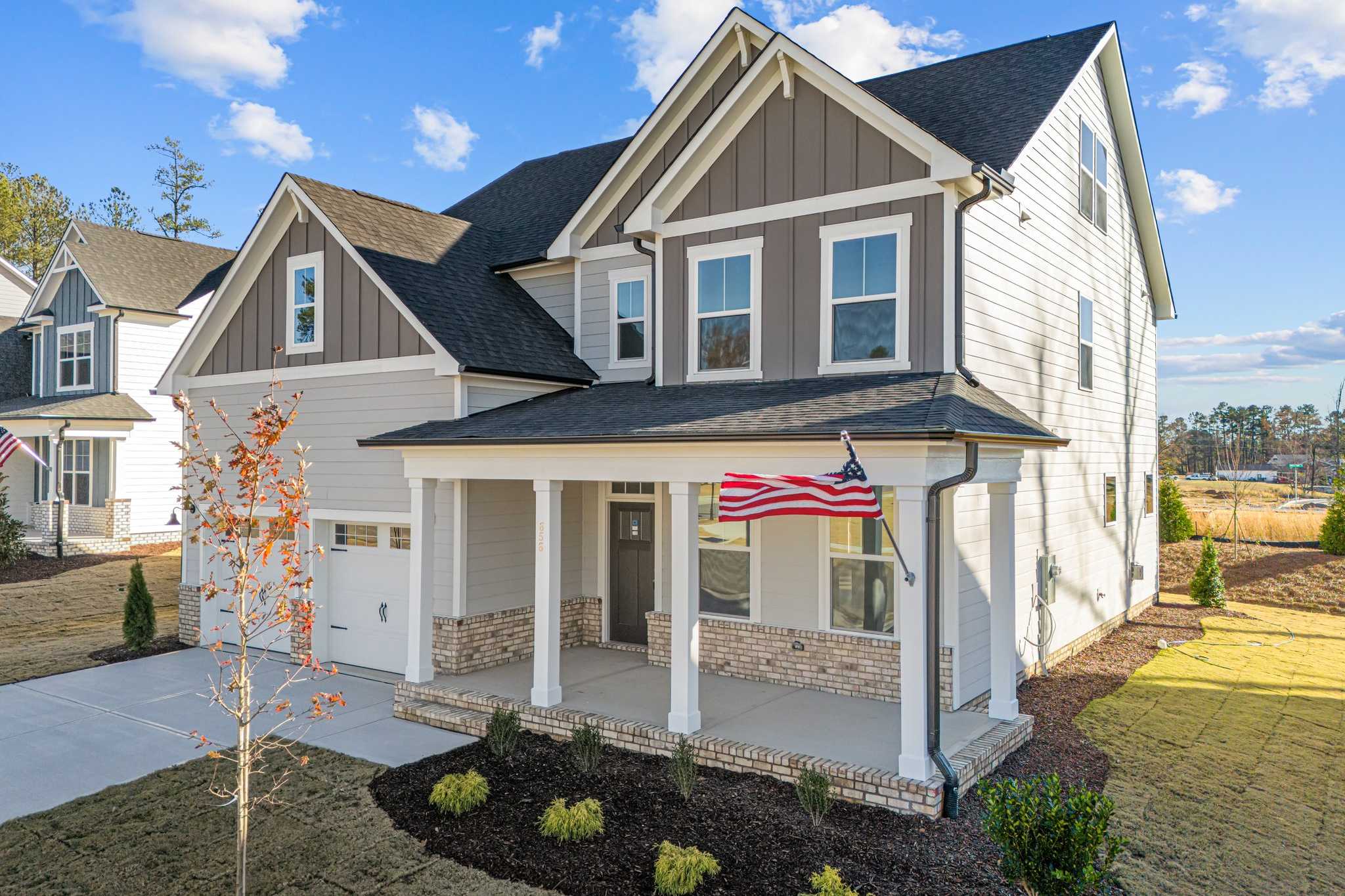 Modern craftsman home exterior at Enclave at Belmont in Belmont NC with covered porch, American flag, and fall landscaping