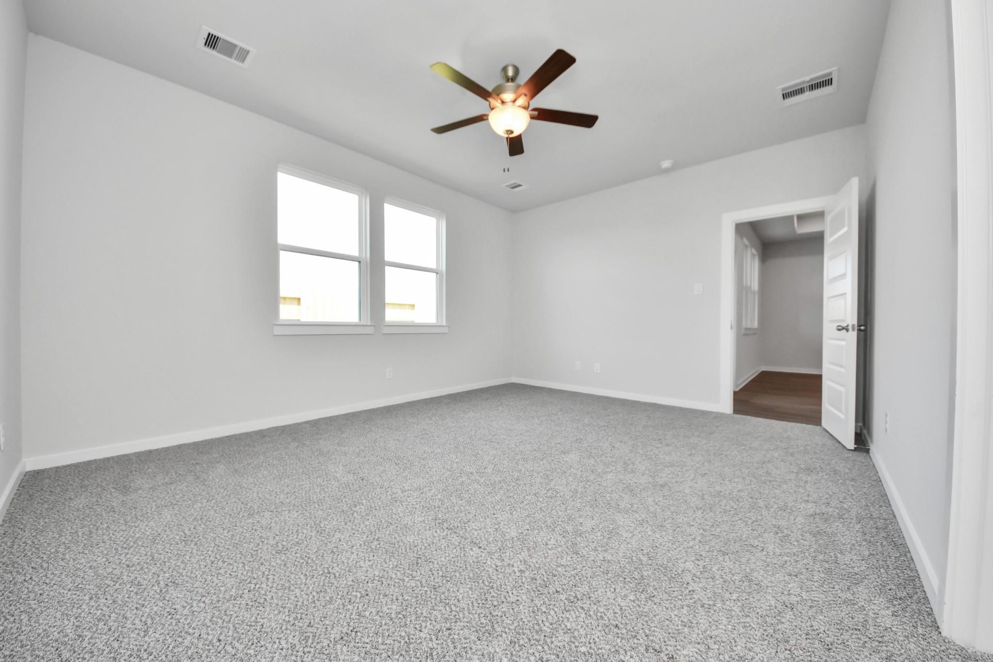 Spacious carpeted bedroom with ceiling fan in The Riviera A floor plan by Davidson Homes in Emberly, Beasley, Texas.