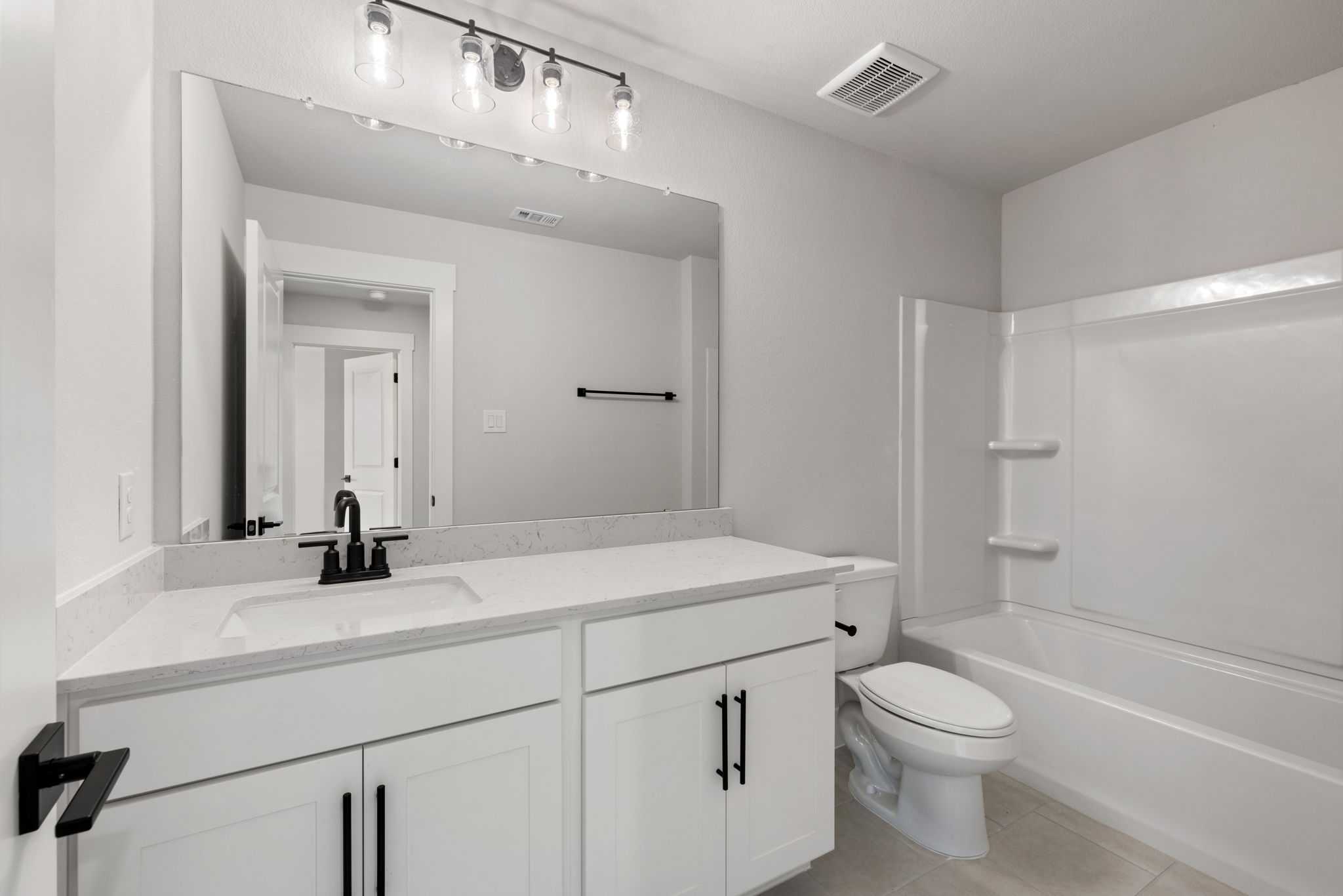 Modern bathroom with white double vanity, large mirror, tub-shower combo in Davidson Homes The Durham E, Wylie, Texas