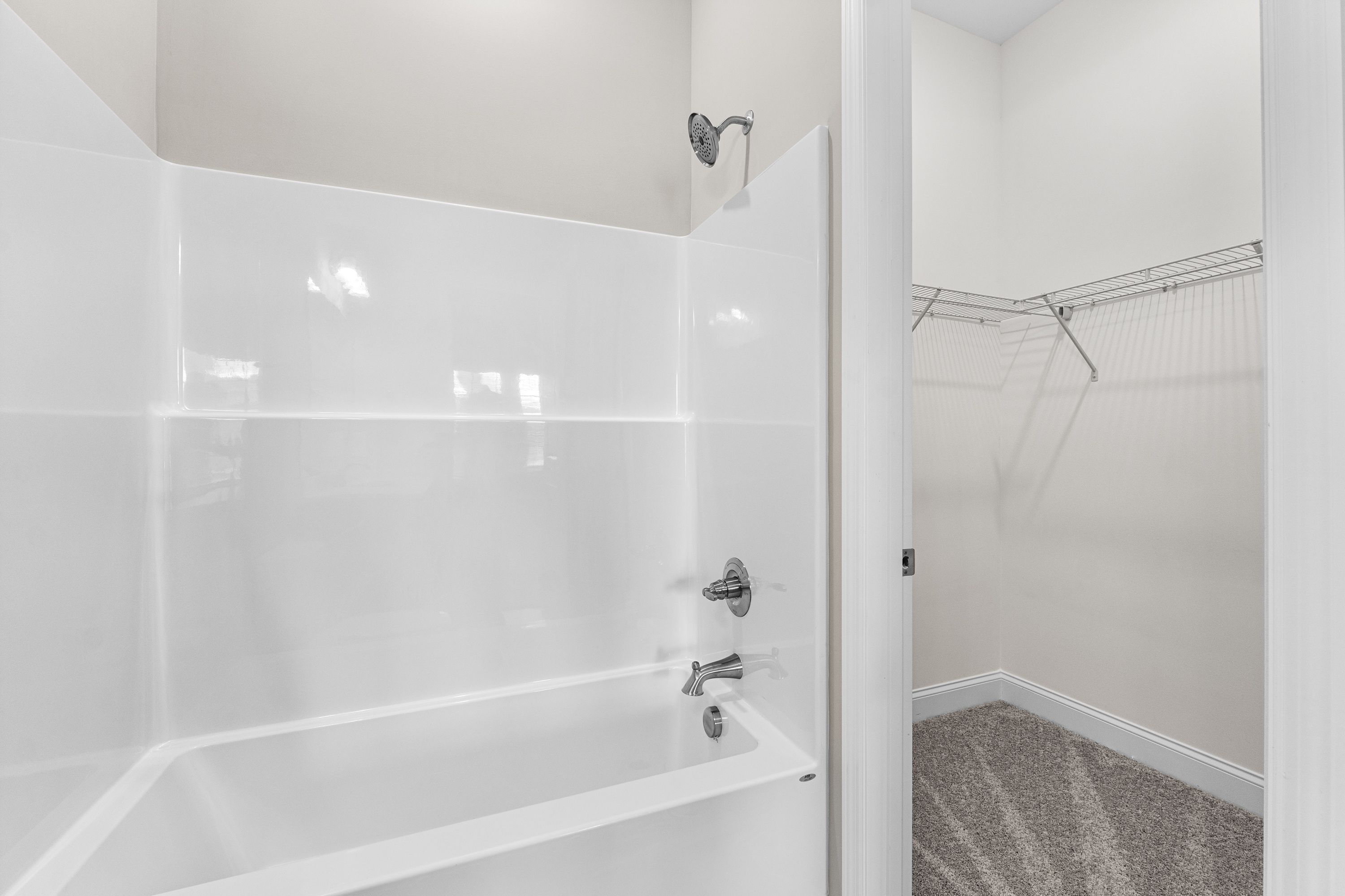 Spacious master bathroom in The Arcadia E featuring white tub, shower, and adjacent walk-in closet with wire shelving