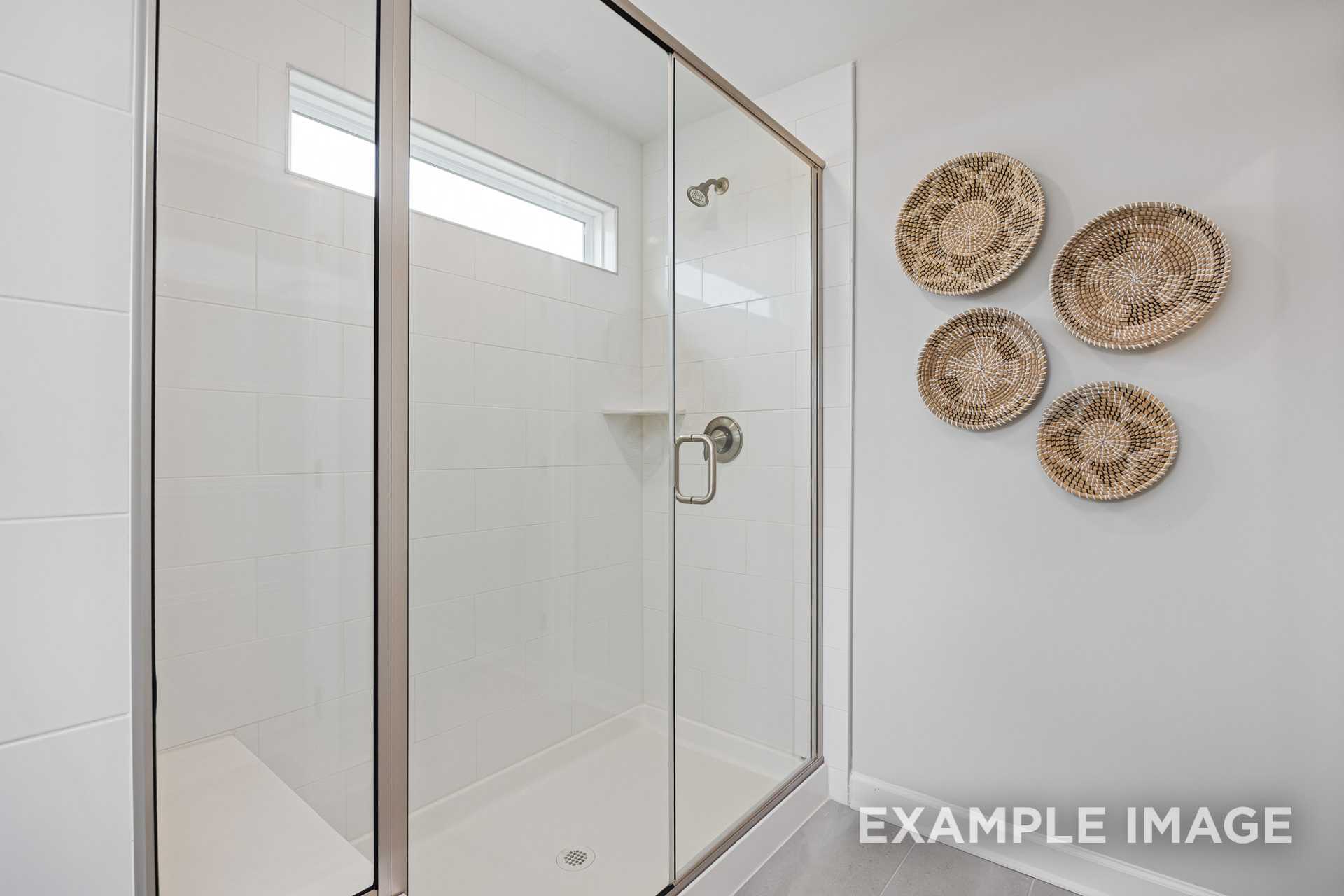 Modern walk-in shower in The Adalynn A master bathroom featuring frameless glass door, white tiles, and woven wall baskets