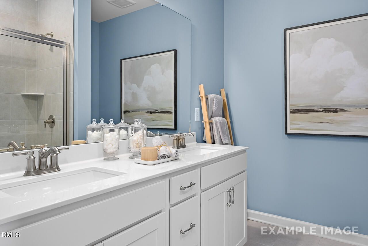 Modern blue master bathroom with double white vanity, glass shower, and abstract wall art in Davidson Homes The Magnolia D, Angier, NC