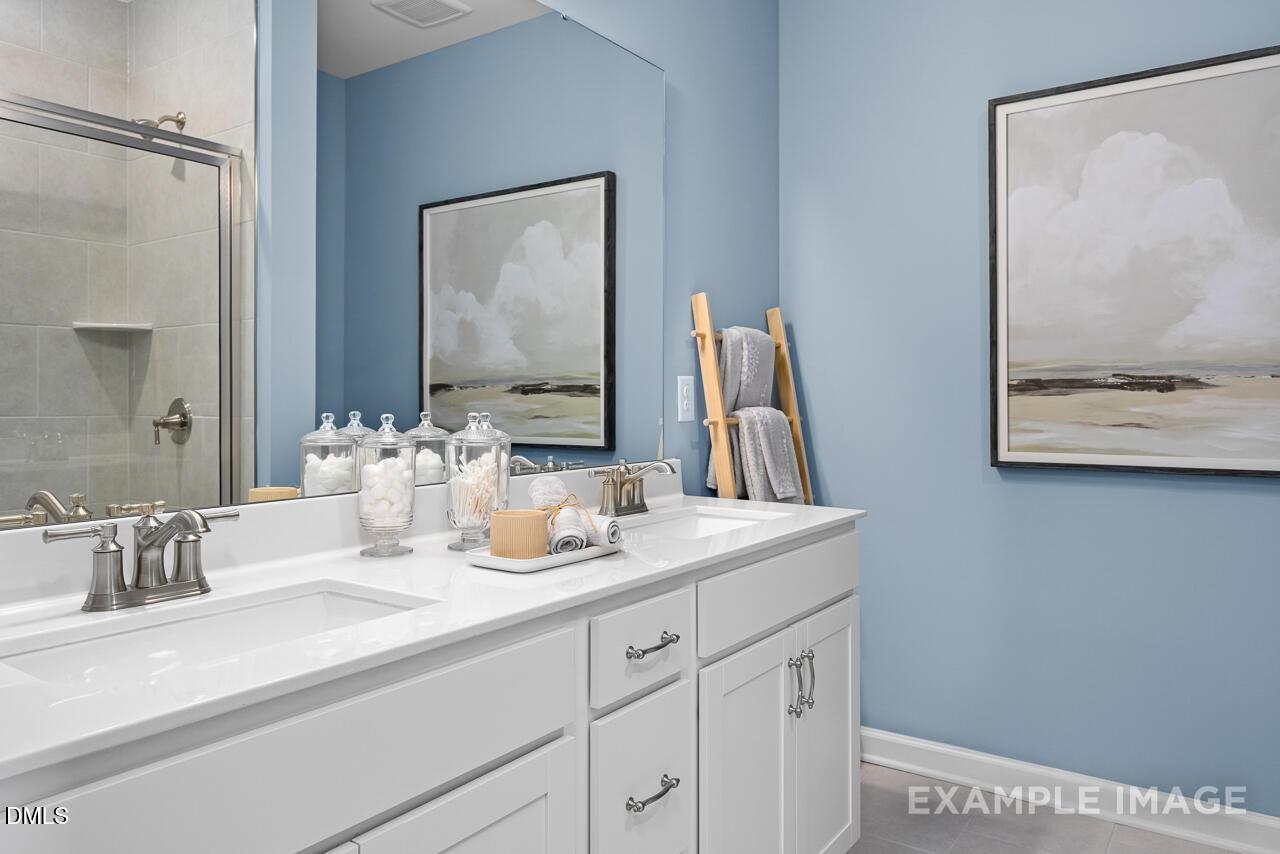 Modern blue master bathroom with double white vanity, glass shower, and abstract wall art in Davidson Homes The Magnolia D, Angier, NC